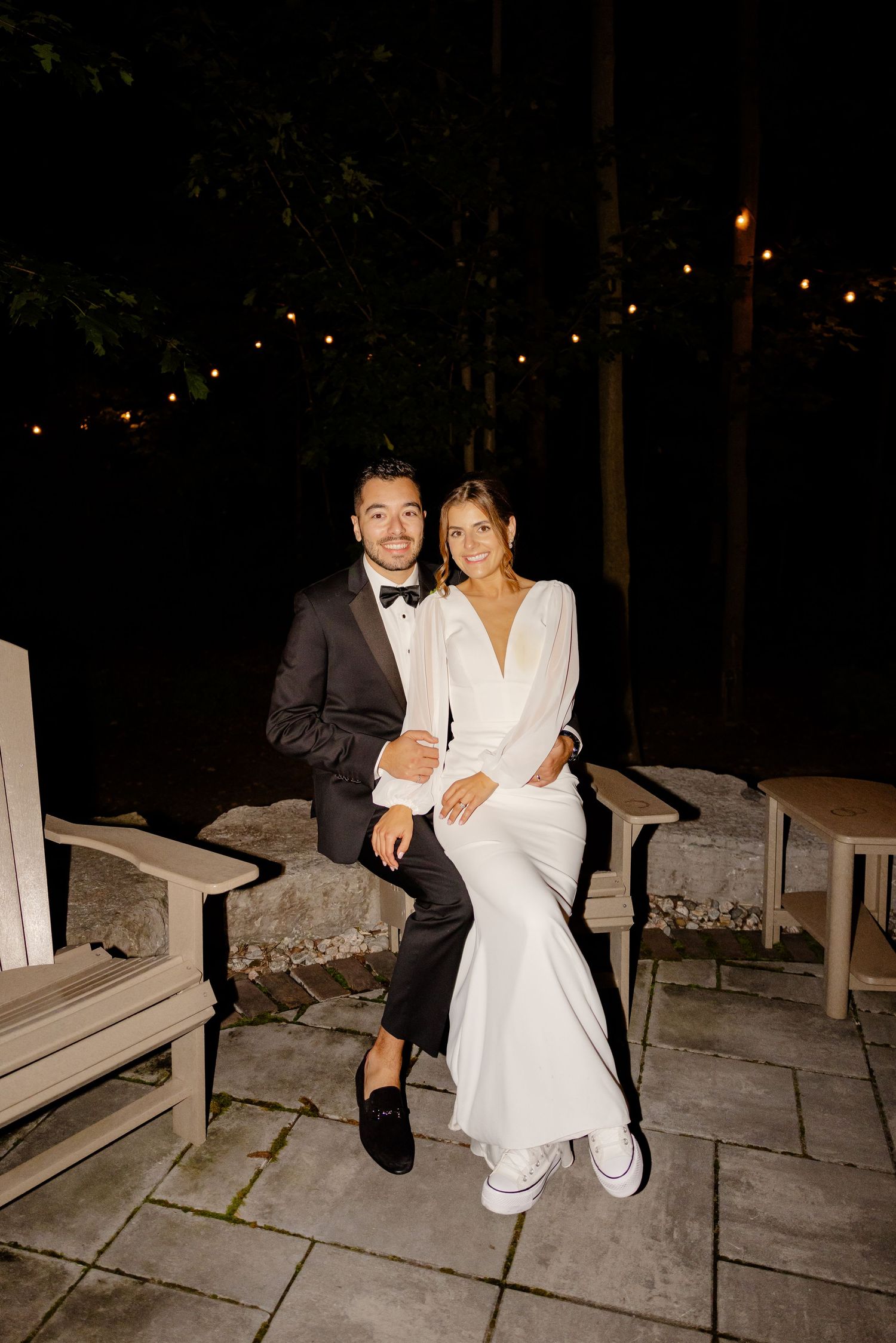 A couple sits together on stone steps during their nighttime wedding celebration.
