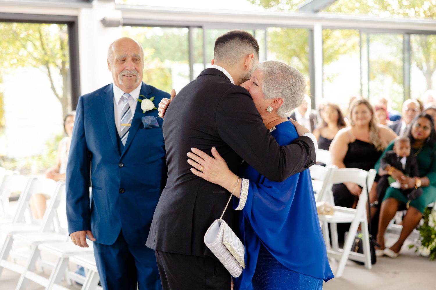 A touching embrace shared during a wedding ceremony entrance in a bright, window-filled venue.