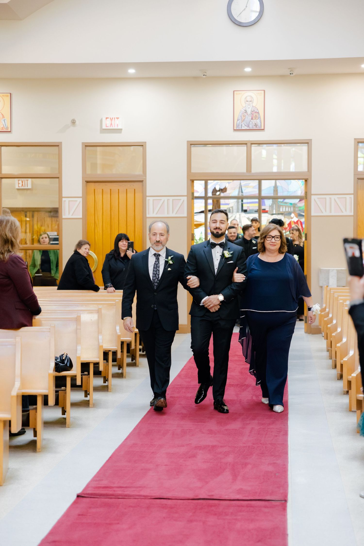 Wedding party walking down red-carpeted church aisle during ceremony processional.