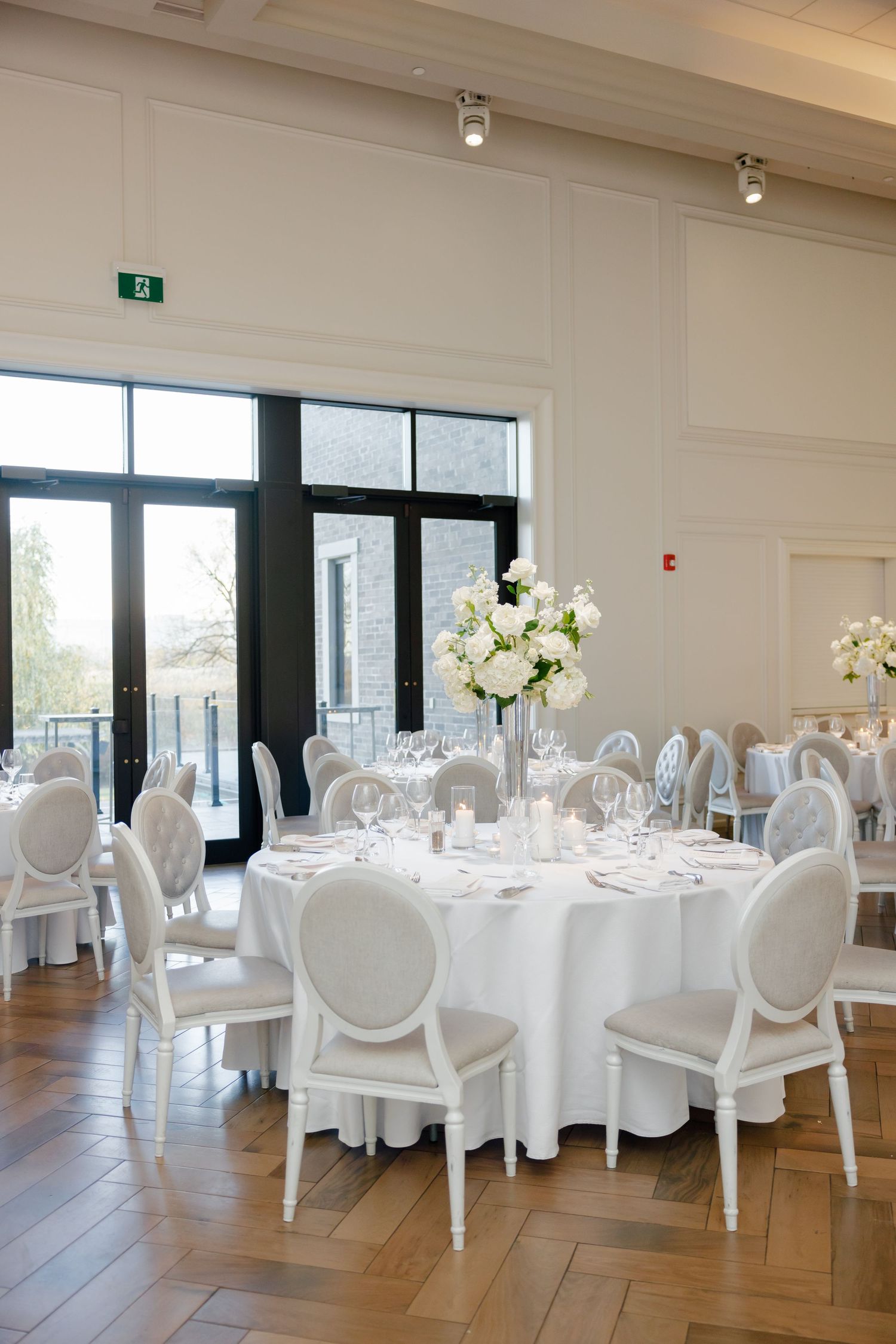 Elegant white wedding reception room with round tables, Louis chairs and tall floral centerpieces.