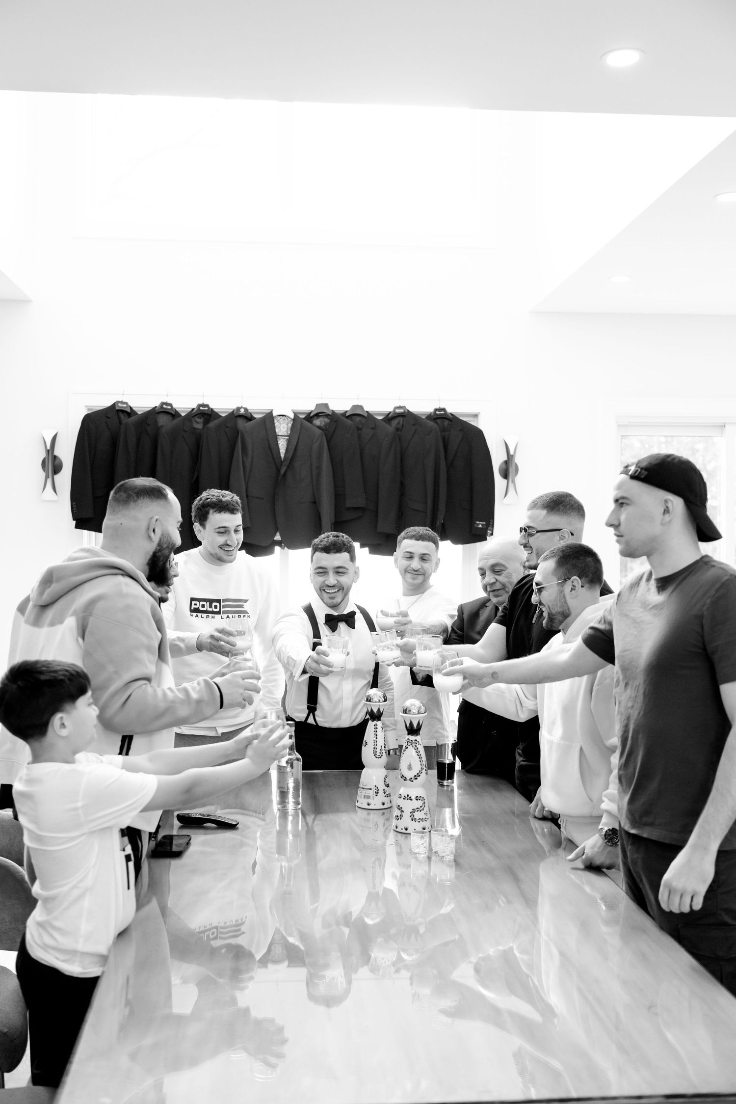 People standing around a glass table during a pre-event gathering with formal suits displayed above.