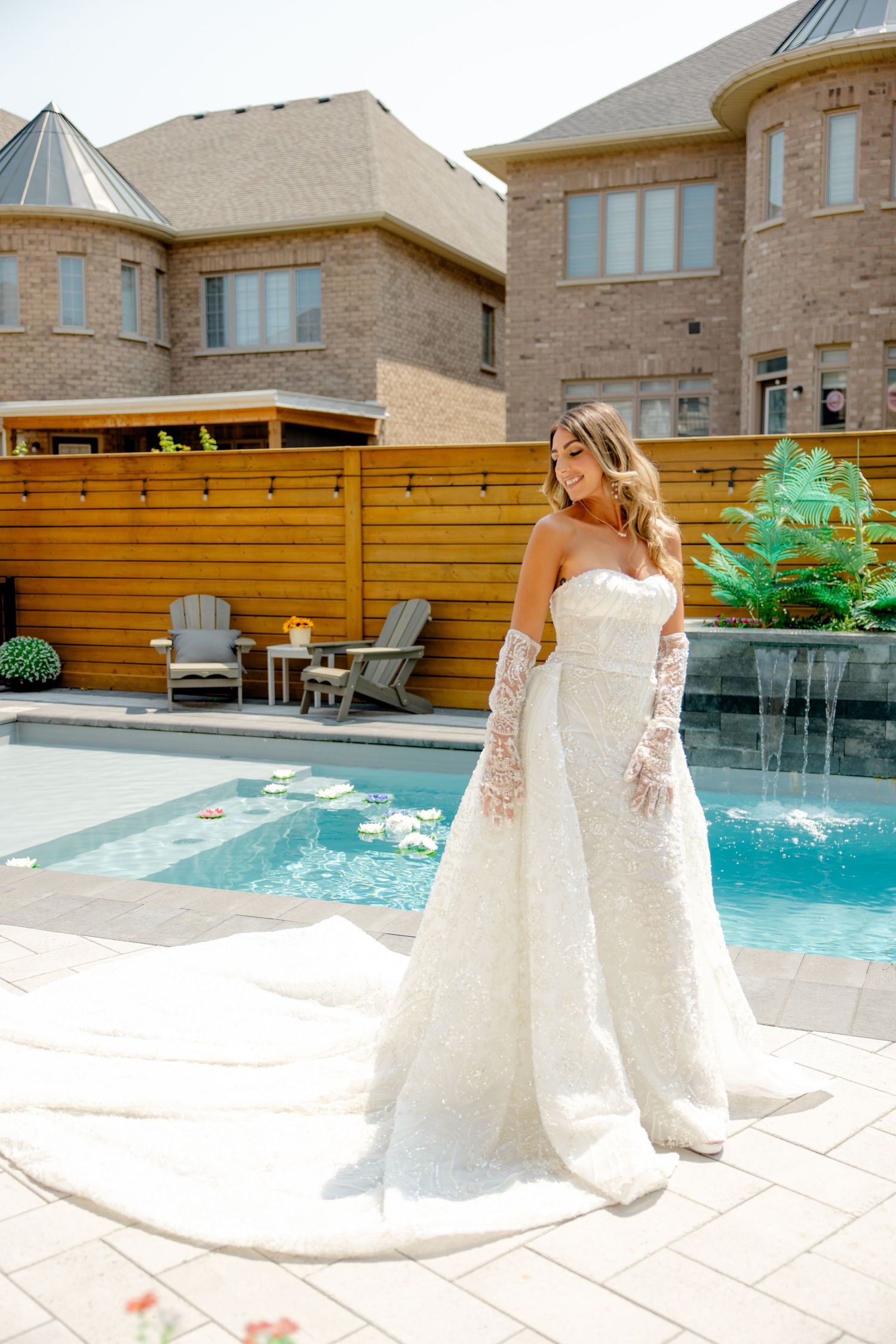 Bridal portrait showcasing lace wedding dress and bouquet against poolside mansion setting.