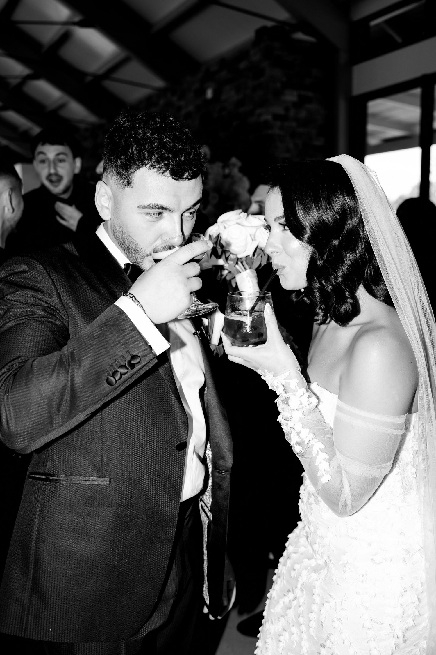 A black and white photo of newlyweds sharing a drink together at their wedding celebration.