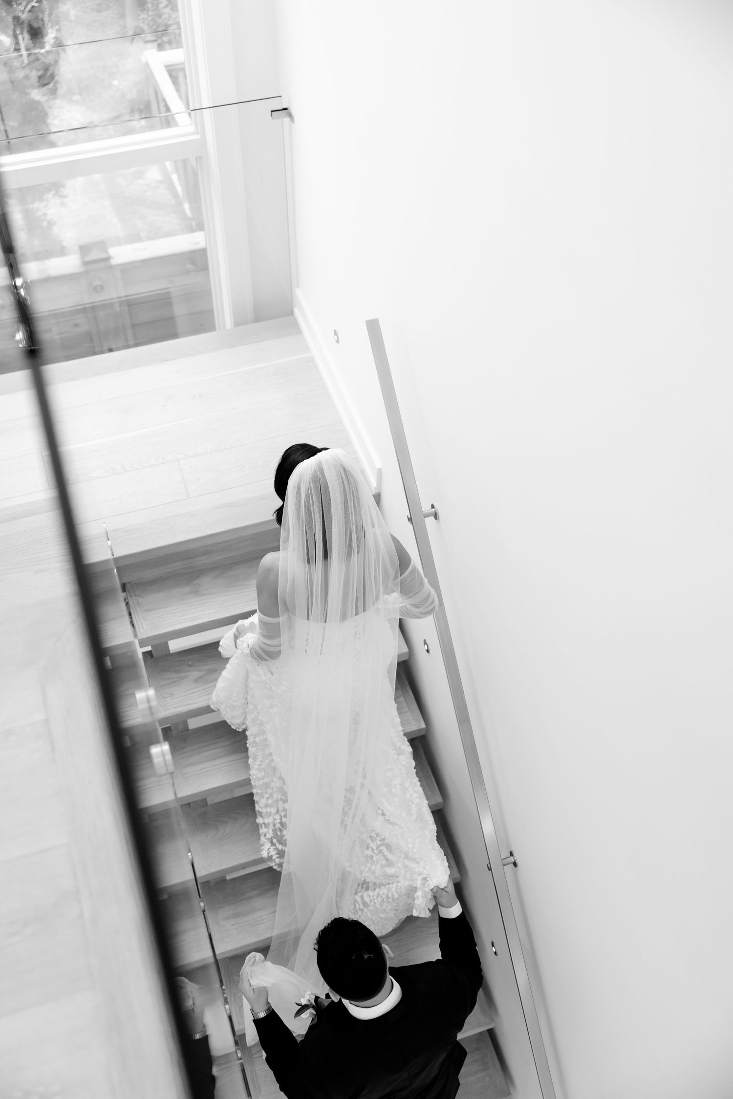 Black and white photo of a couple descending stairs, bride's lace dress trailing behind.