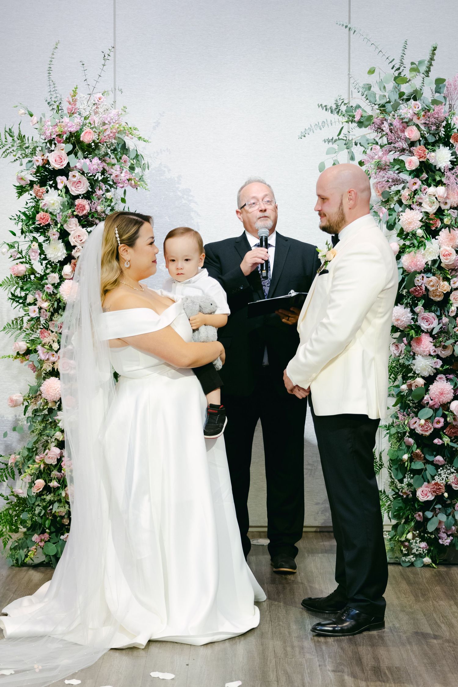 Wedding ceremony with officiant speaking between pink floral arrangements.