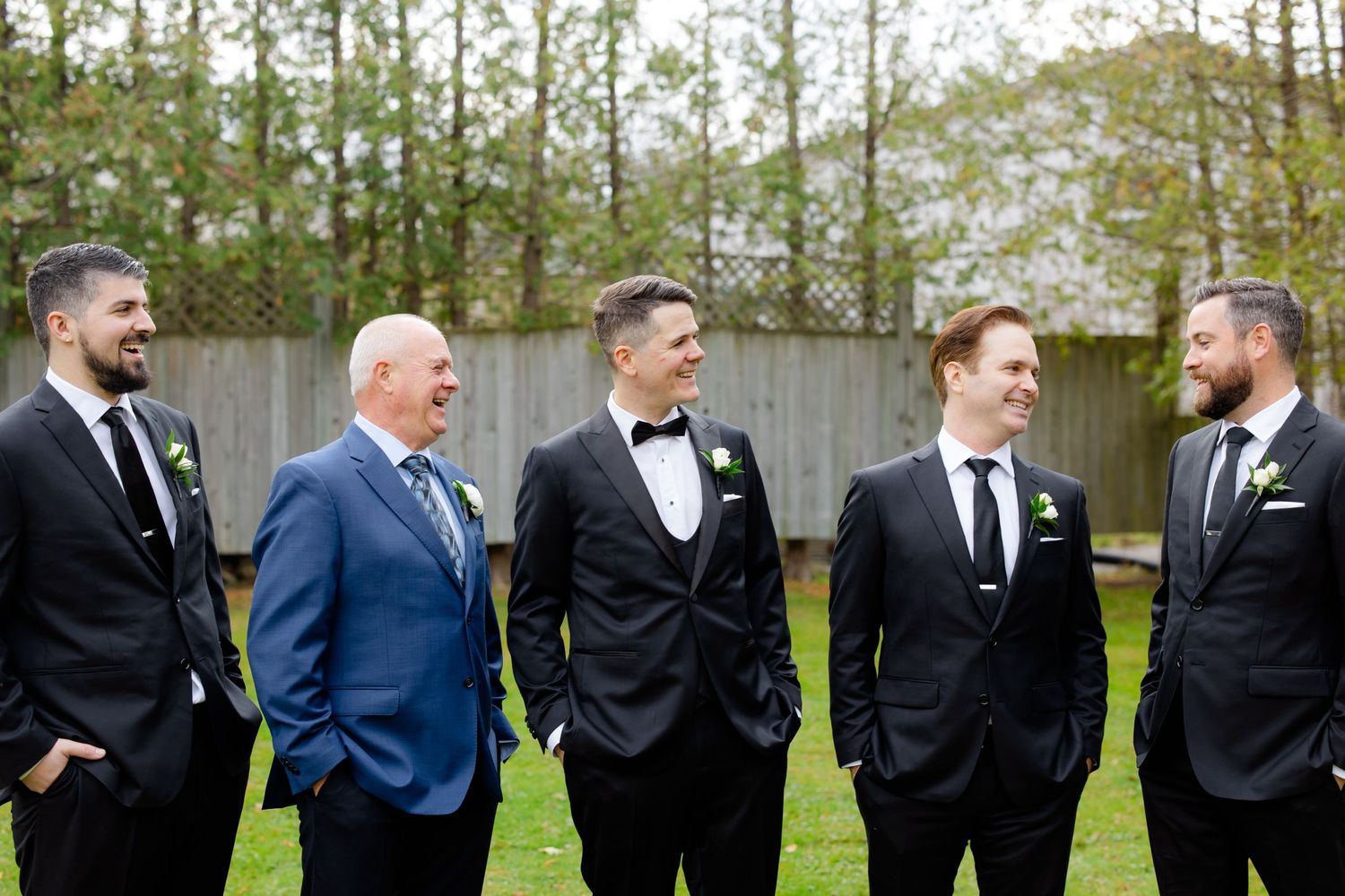 Five people in formal attire share a candid moment together outdoors.