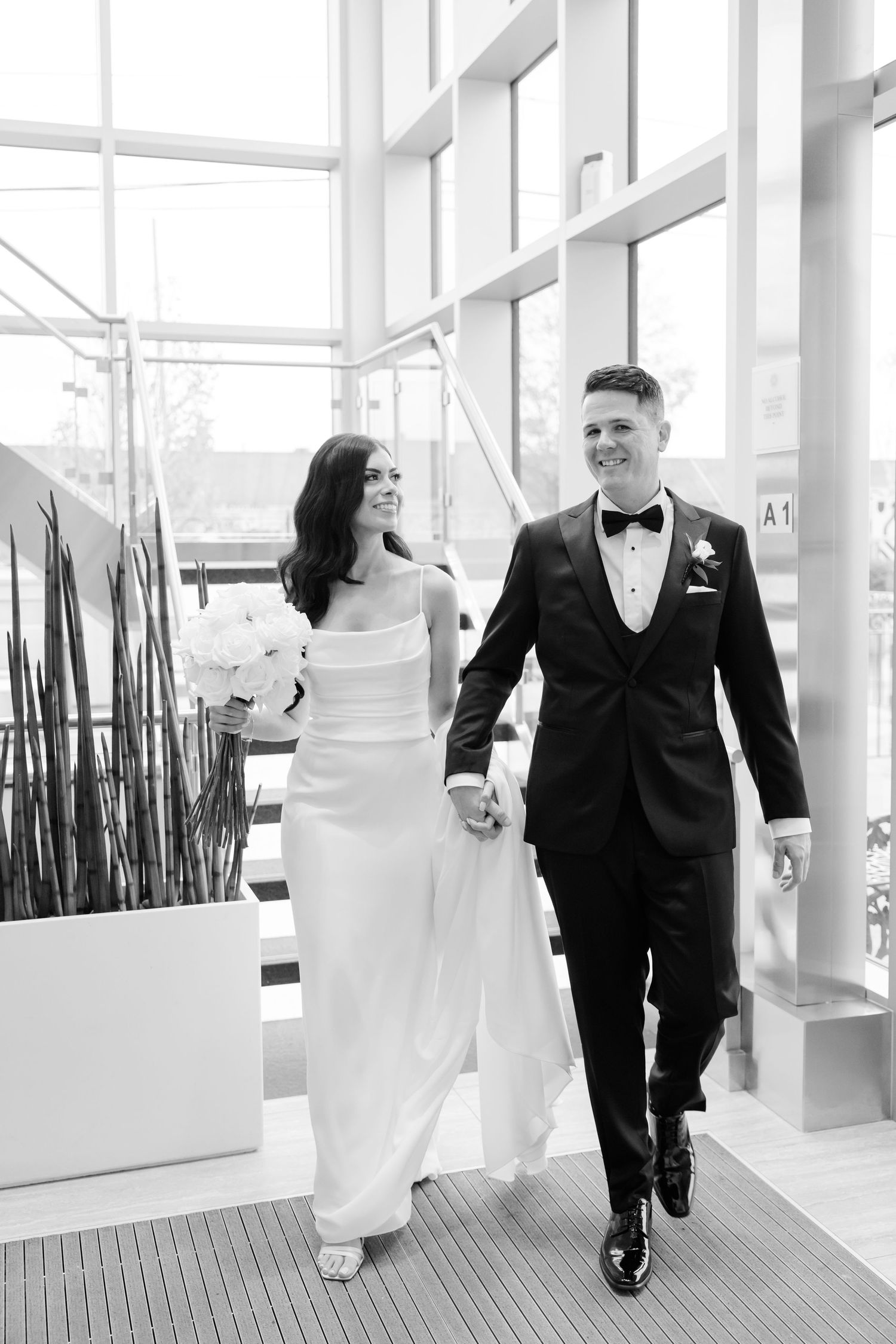 Joyful wedding couple walking through bright modern space with indoor greenery.