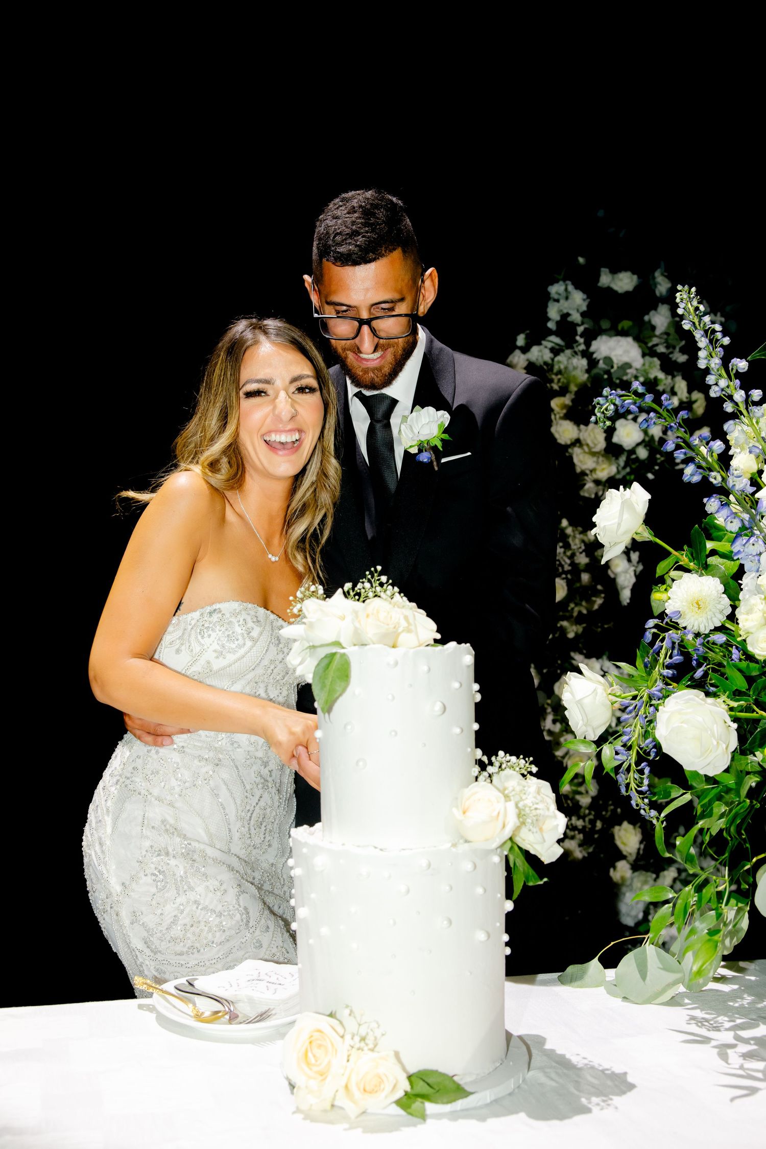 Joyful wedding moment captured during cake cutting ceremony with floral decorations.