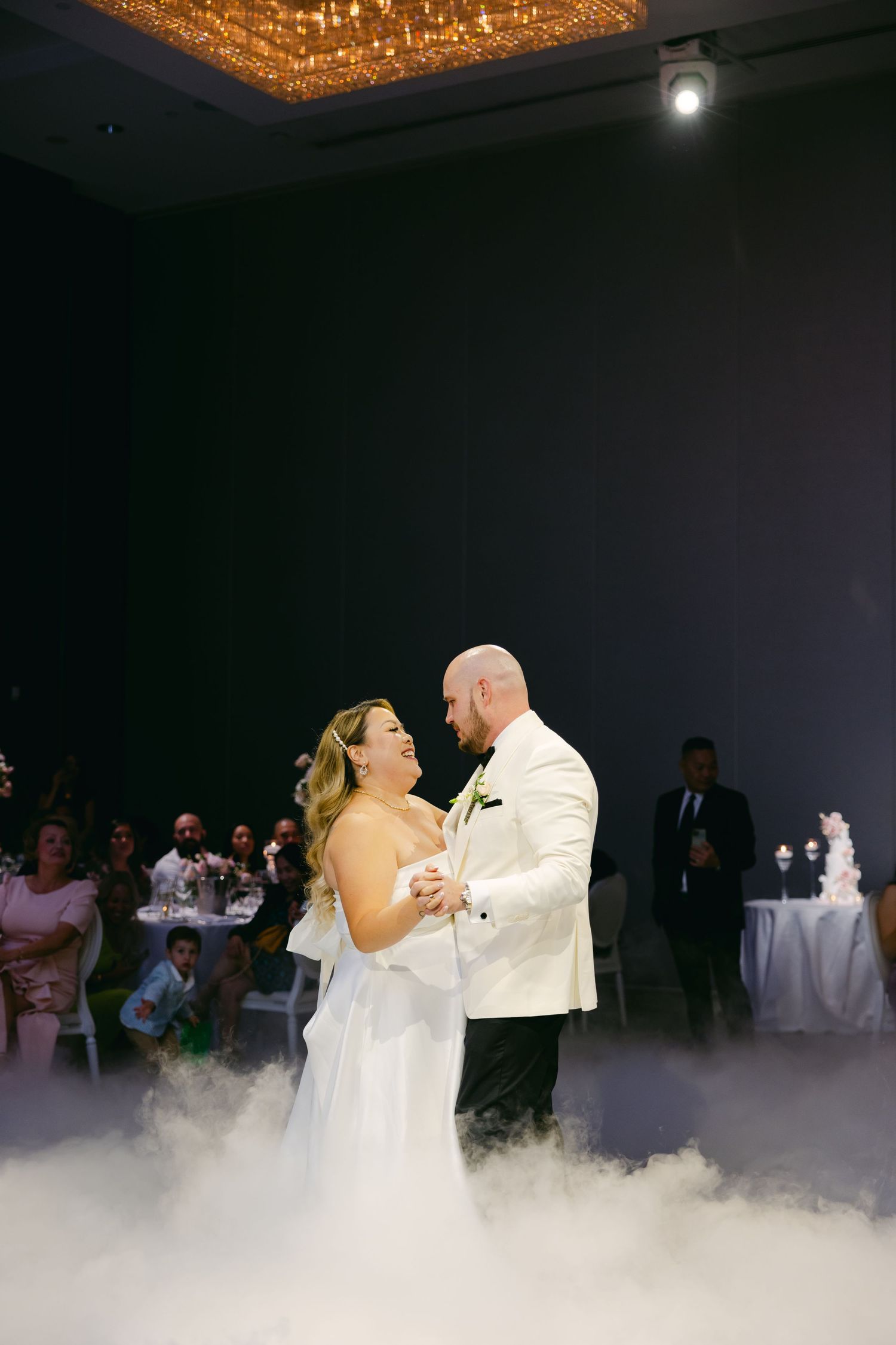 Couple shares an intimate dance moment surrounded by elegant fog effects and chandelier lighting.
