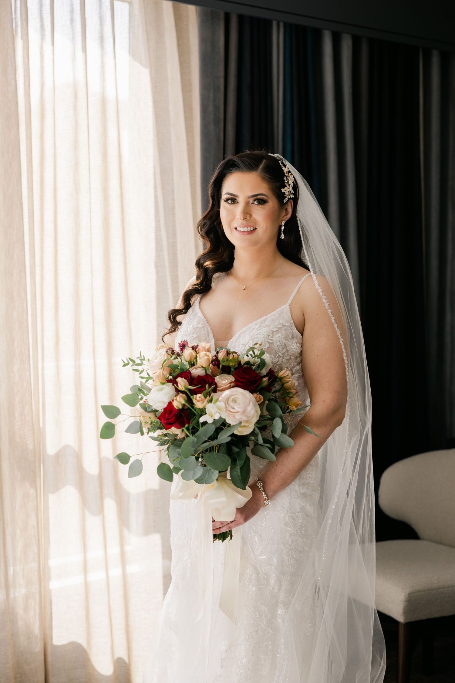 Side-lit bridal portrait with lace gown, long veil and mixed flower bouquet.