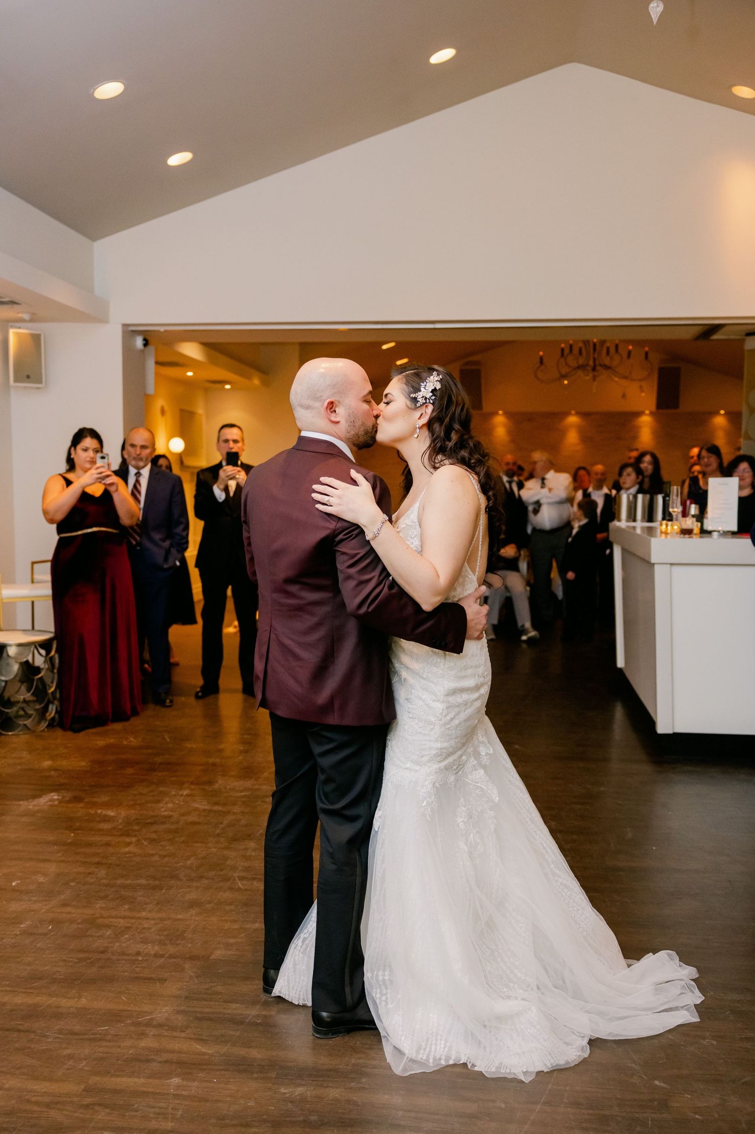 Couple sharing first dance while wedding guests watch and take photos.