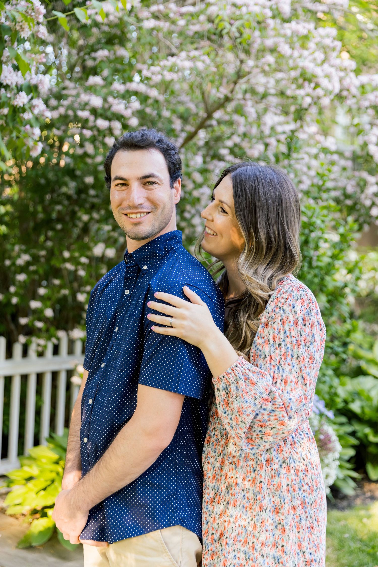 A couple shares a joyful moment together in a spring garden with white flowers.