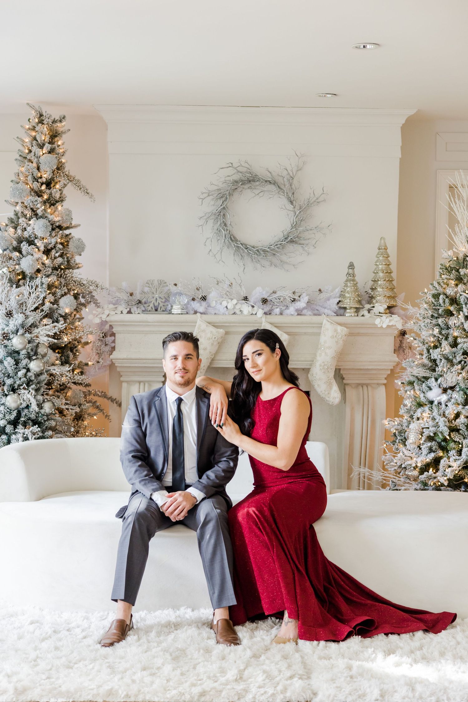 Romantic holiday photoshoot featuring couple in red and grey attire against winter white Christmas backdrop.