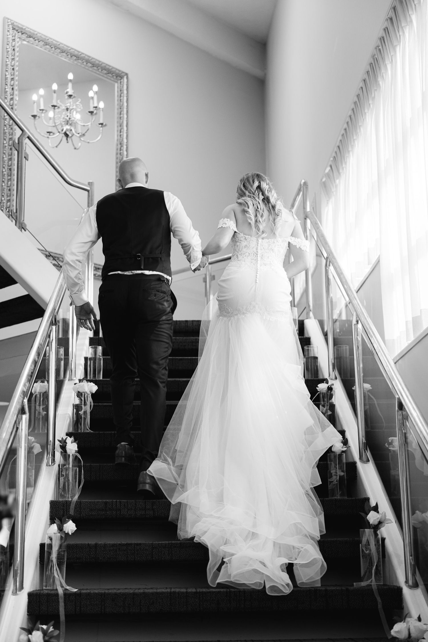 Black and white wedding photo of couple ascending decorated staircase.