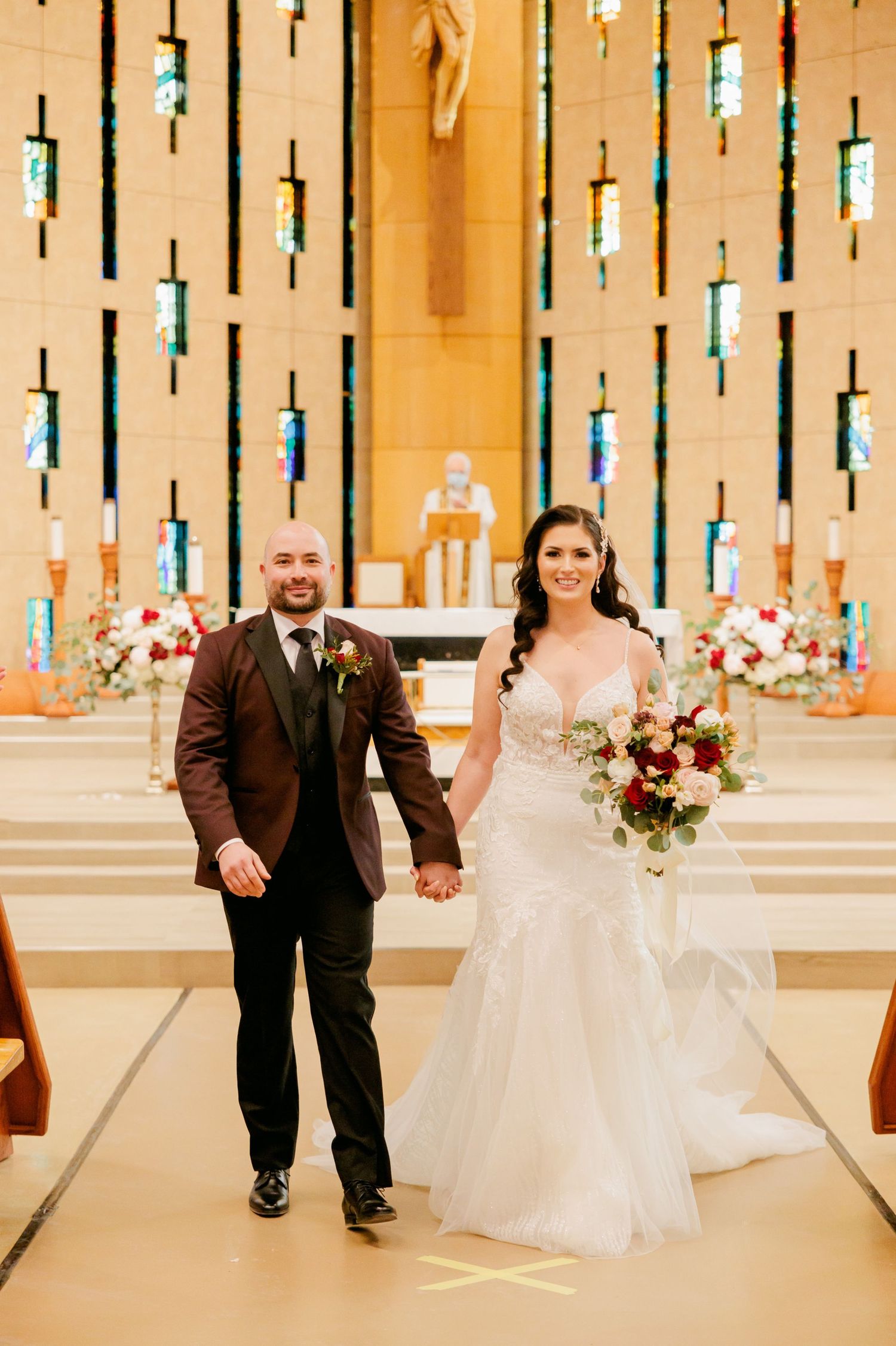 Wedding ceremony in modern church with vertical stained glass windows and floral arrangements.