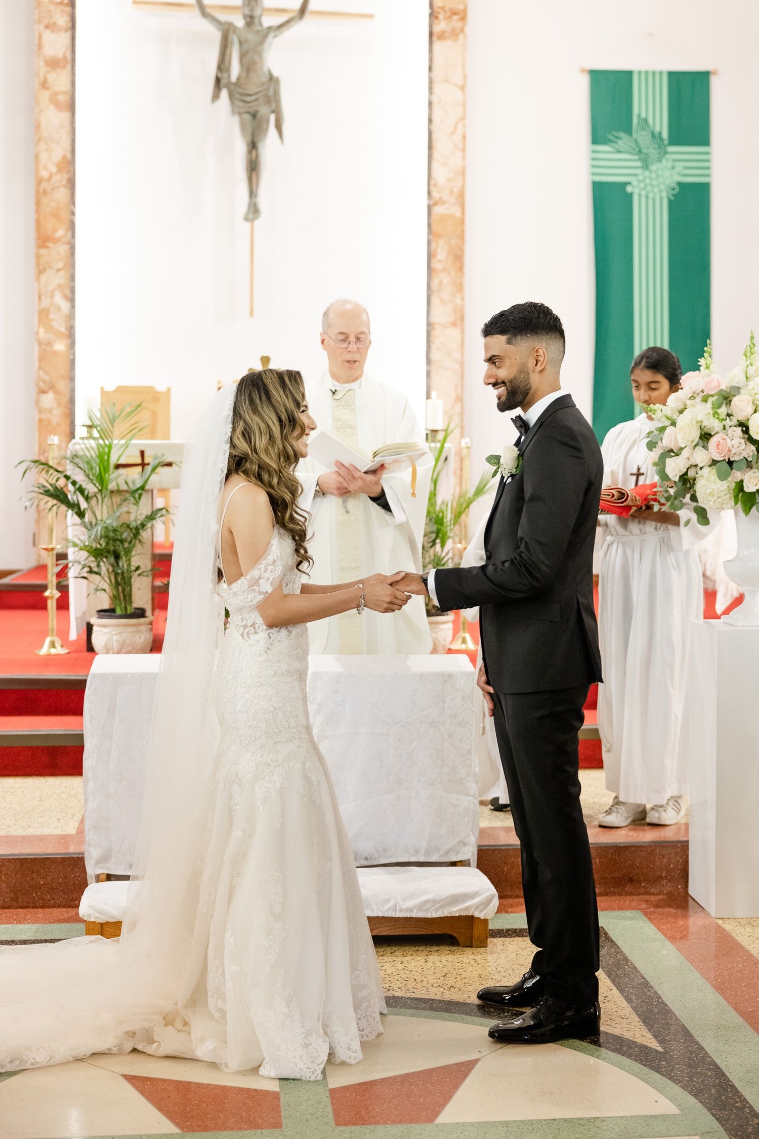 An intimate wedding ceremony moment in front of a crucifix with green banners and white flowers.