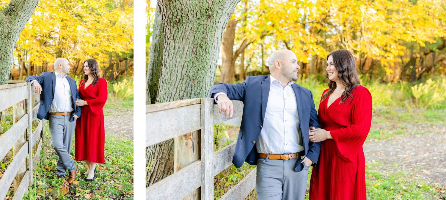 Couple in formal attire pose by wooden fence with golden fall foliage in background.
