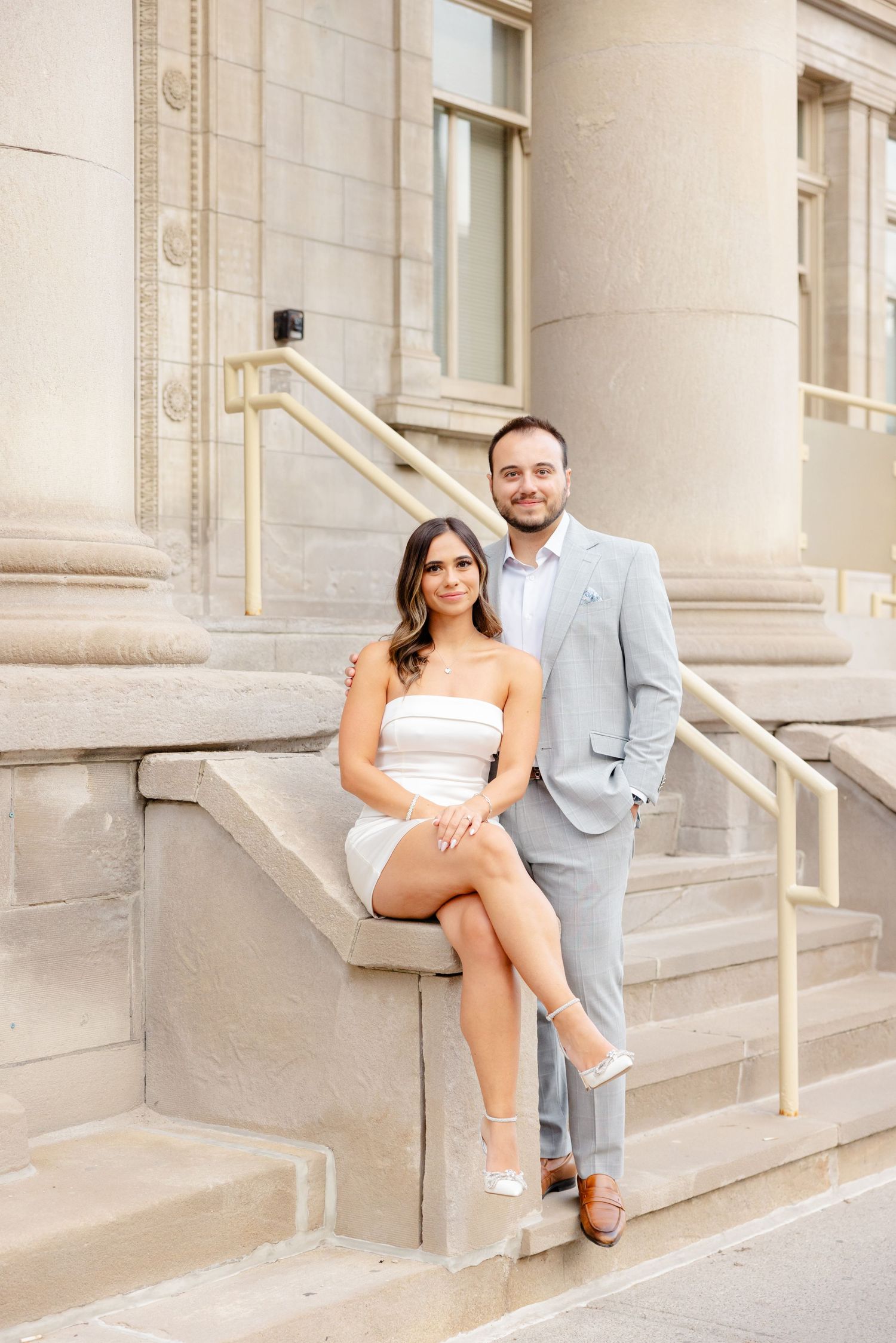 A couple poses together on the steps of a historic building with architectural details.