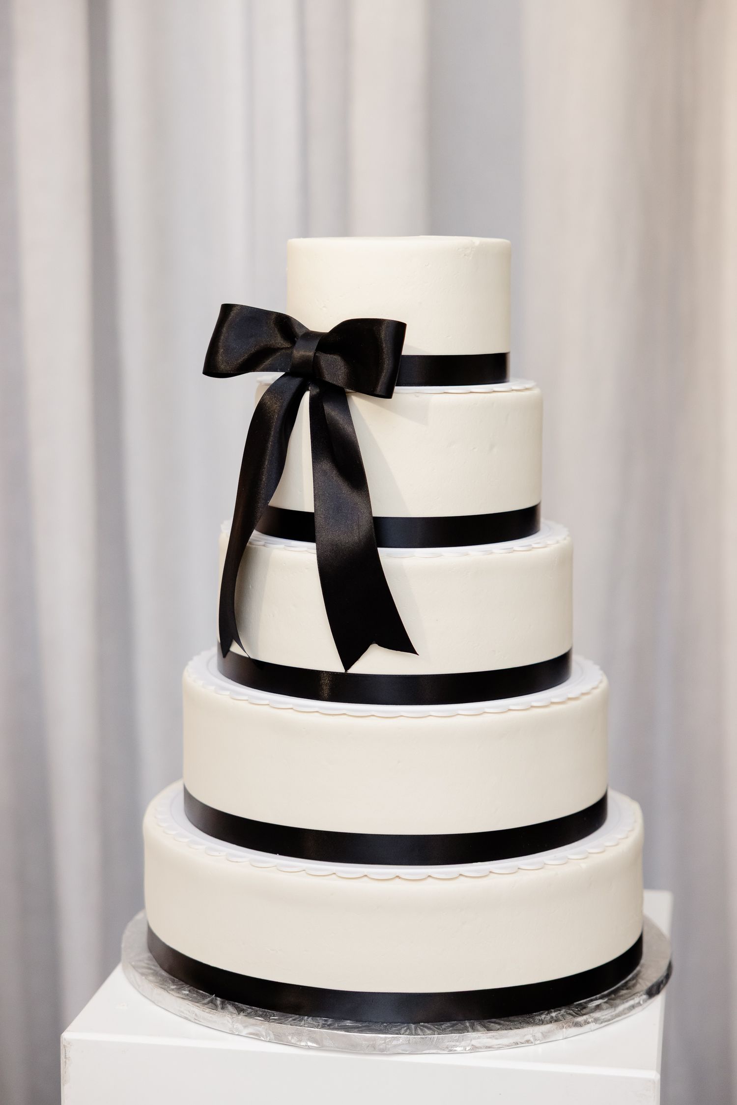 Elegant five-tier white wedding cake with black ribbon trim and large black bow accent on display.