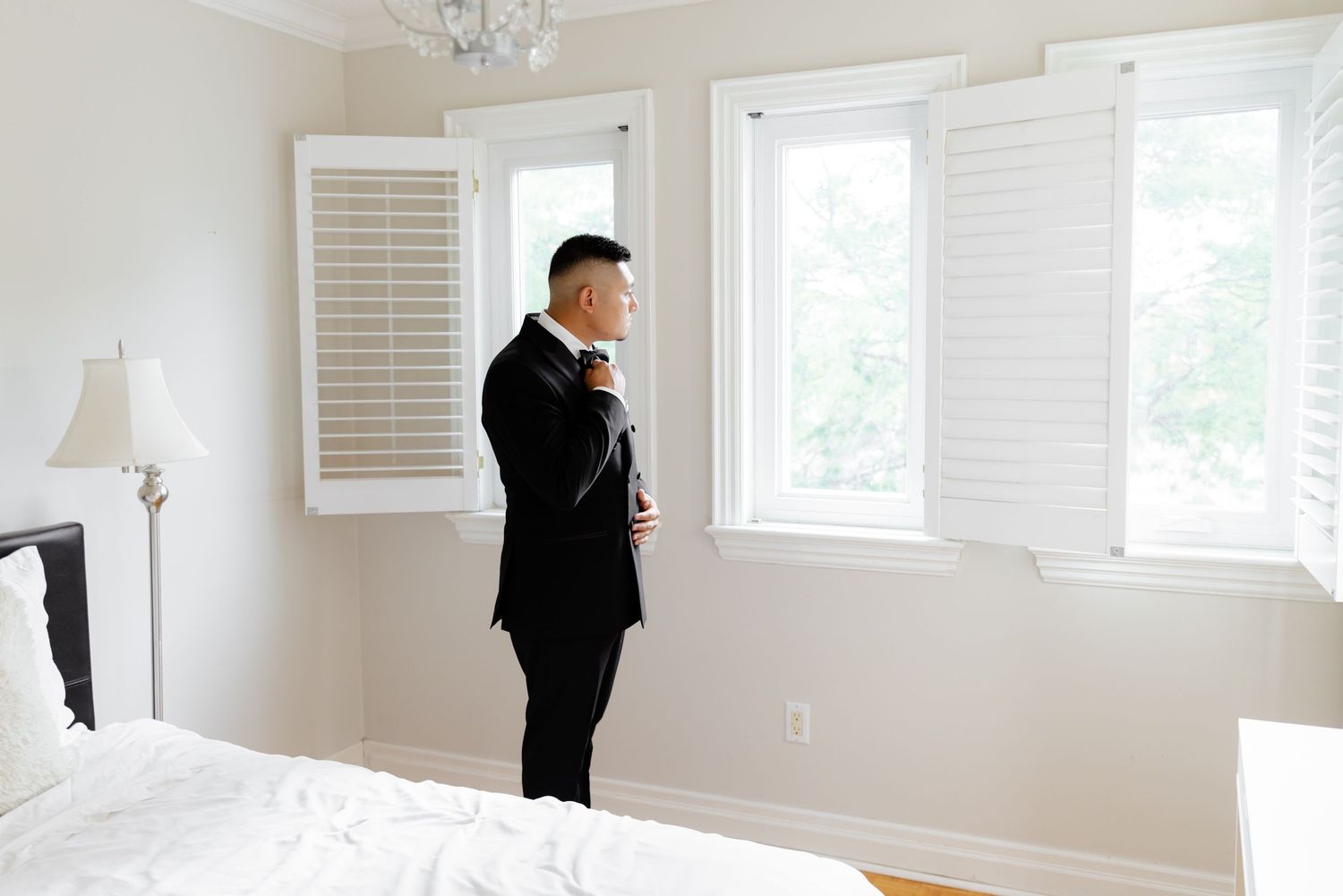 A bright white interior room with window shutters and an elegant crystal chandelier hanging from the ceiling.