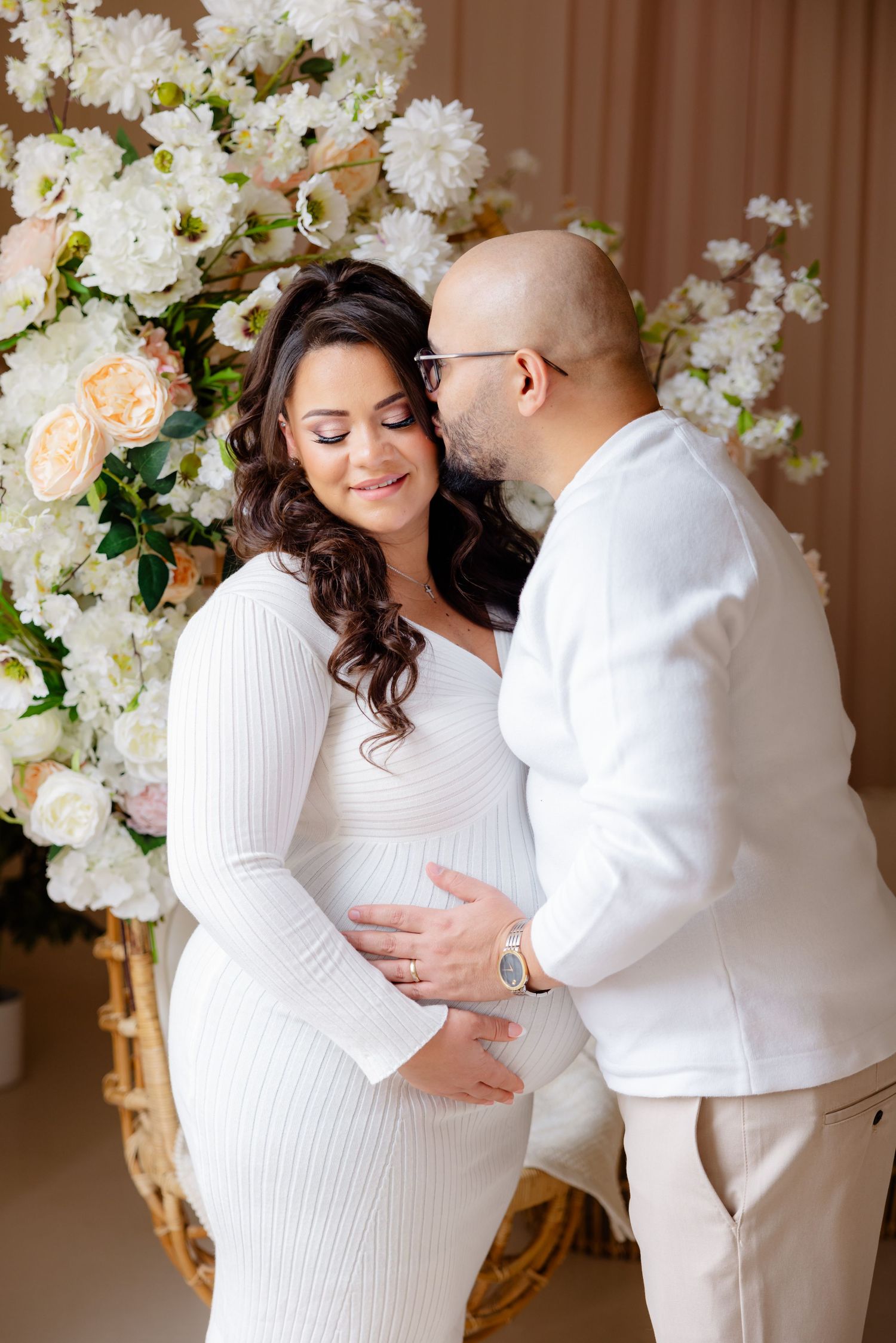 Romantic maternity photo with white floral backdrop and soft lighting.