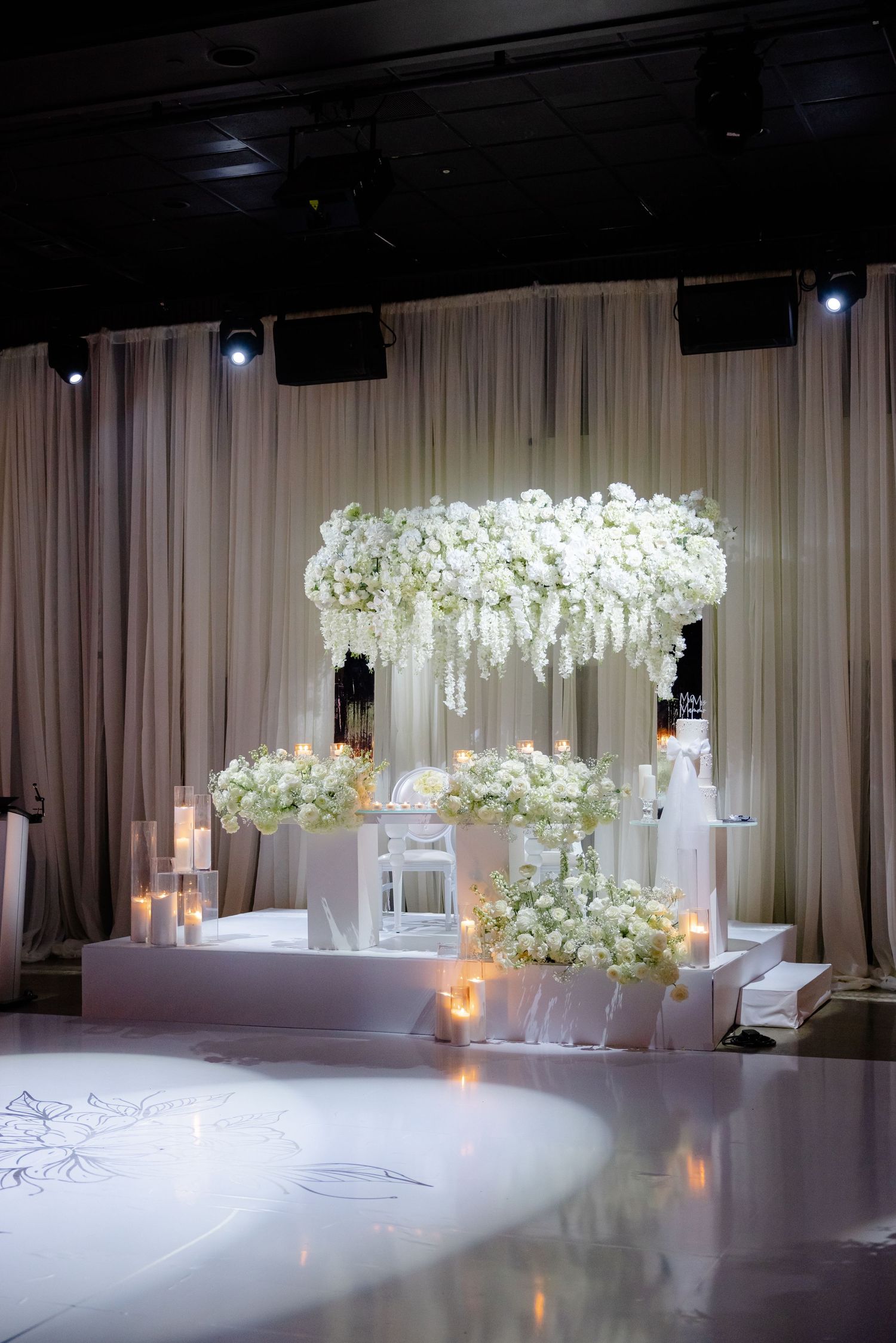 Dramatic wedding ceremony setup with suspended floral chandelier and white floral arrangements on pedestals.