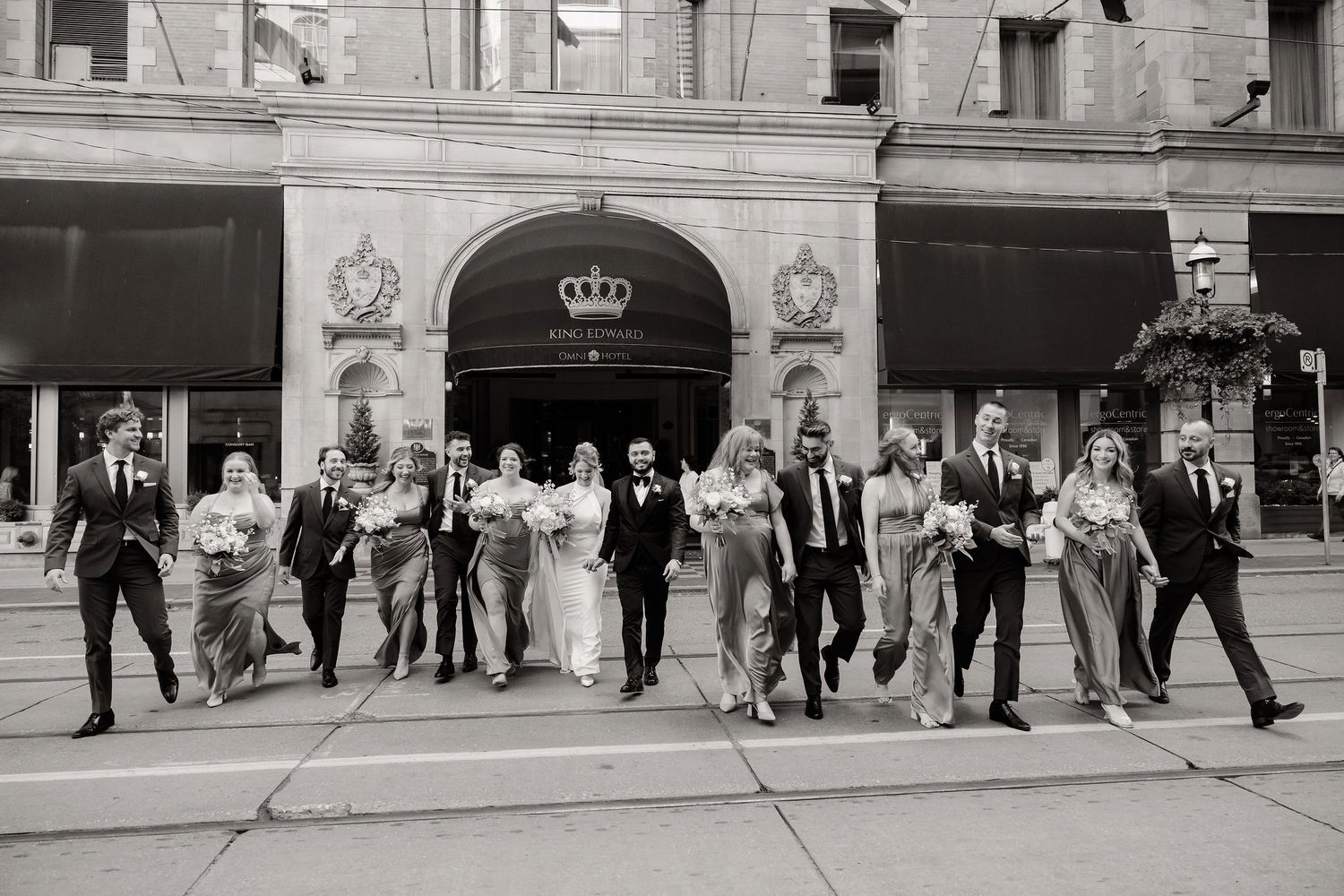Wedding party members line up for a group photo outside a historic hotel entrance.