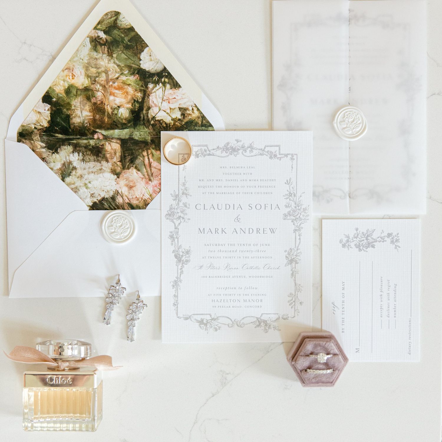 Elegant wedding invitation suite with floral envelope liner and perfume bottle on marble surface.