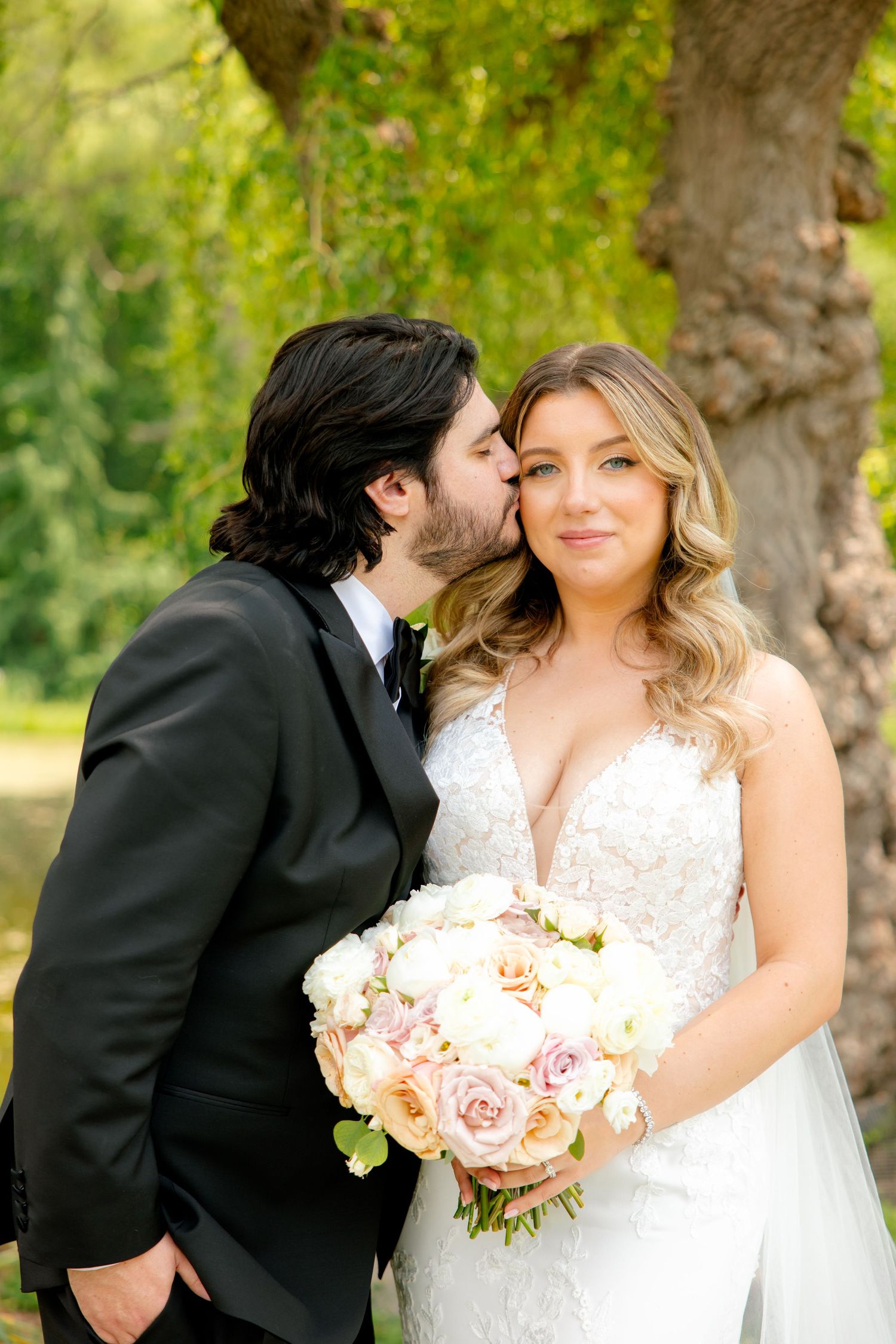Intimate wedding moment captured under willow tree with bride holding pink and white bouquet.