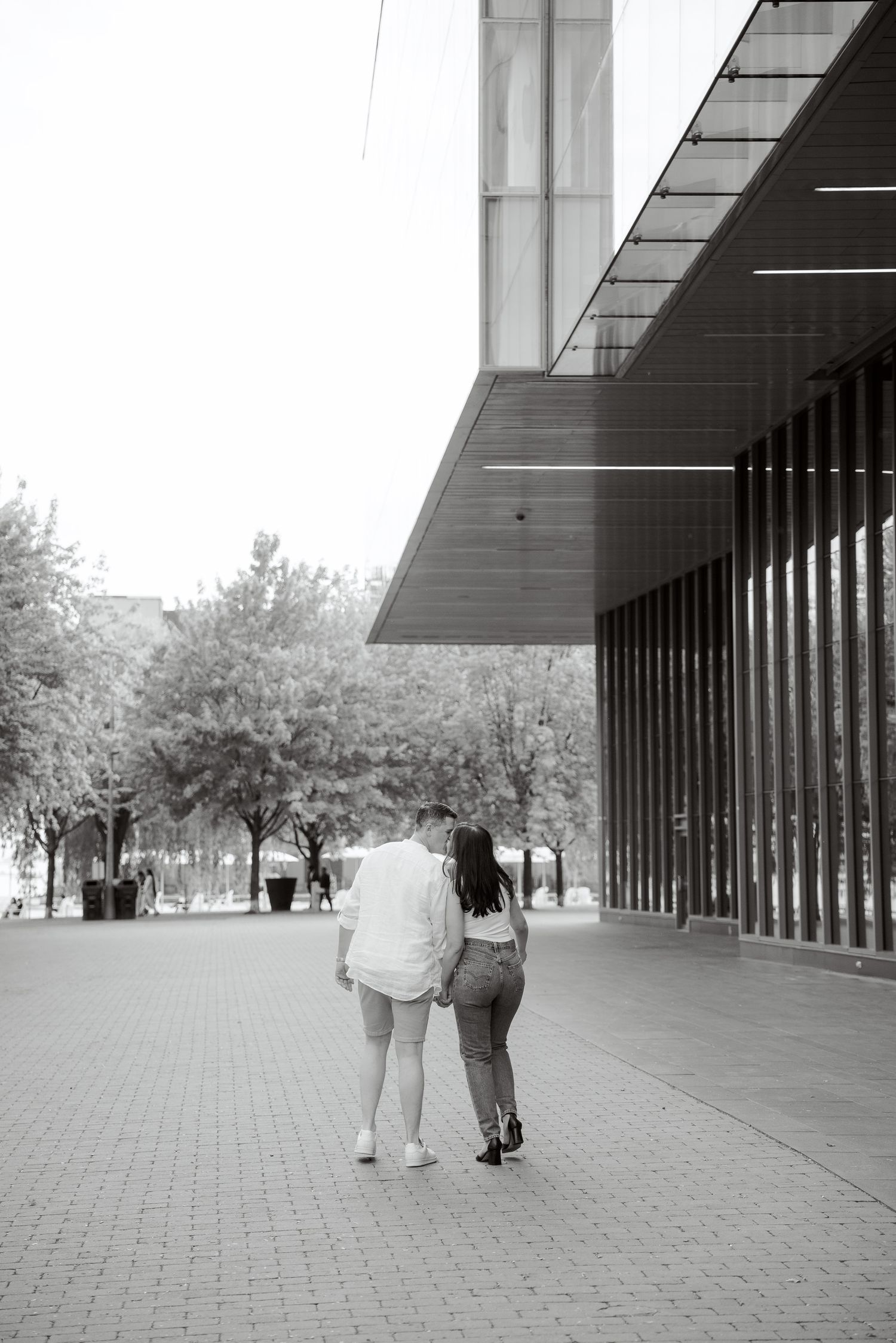 A black and white photo of a couple walking along a modern building exterior.