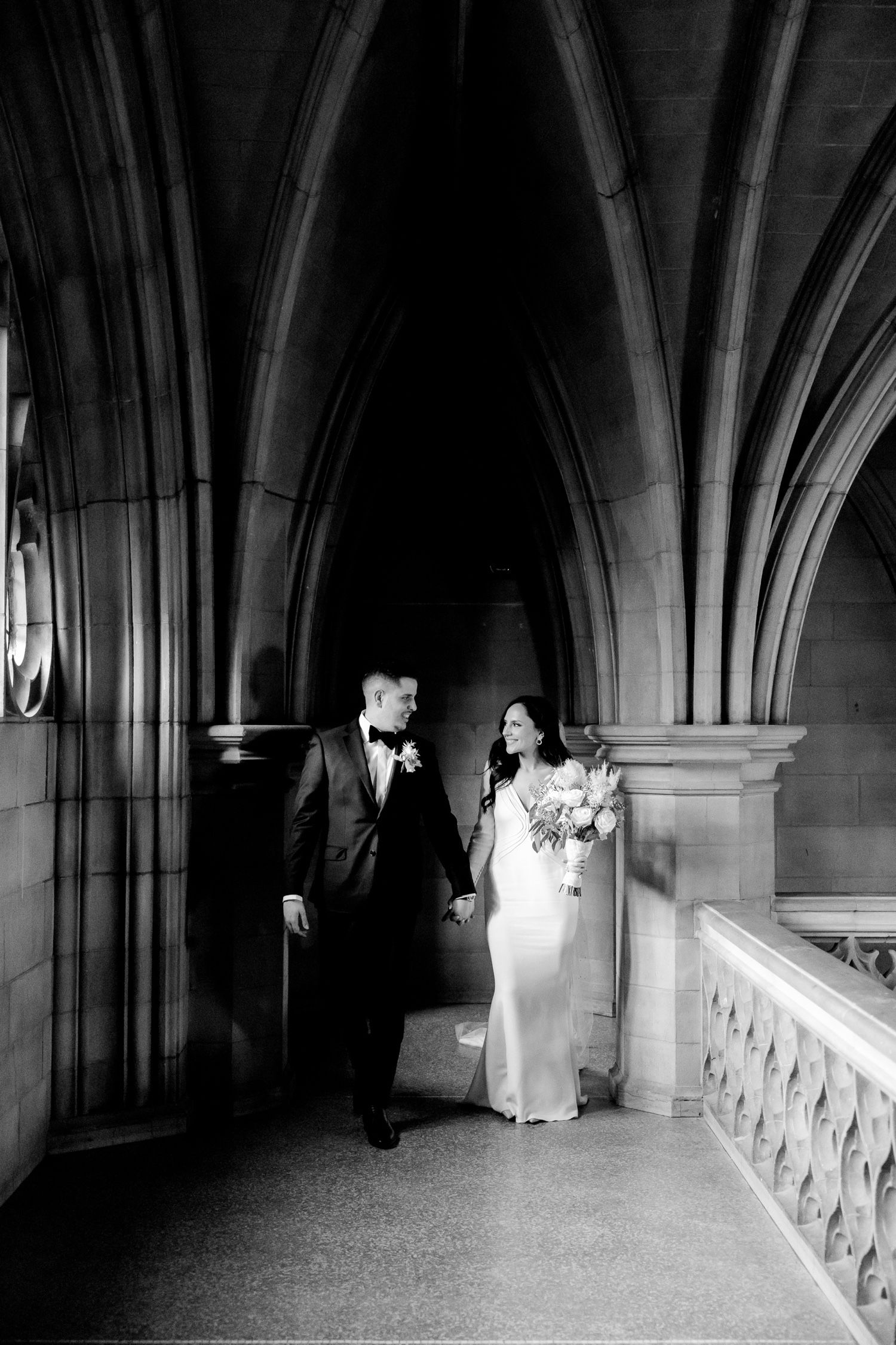 Black and white wedding photo under Gothic stone arches and vaulted ceiling.