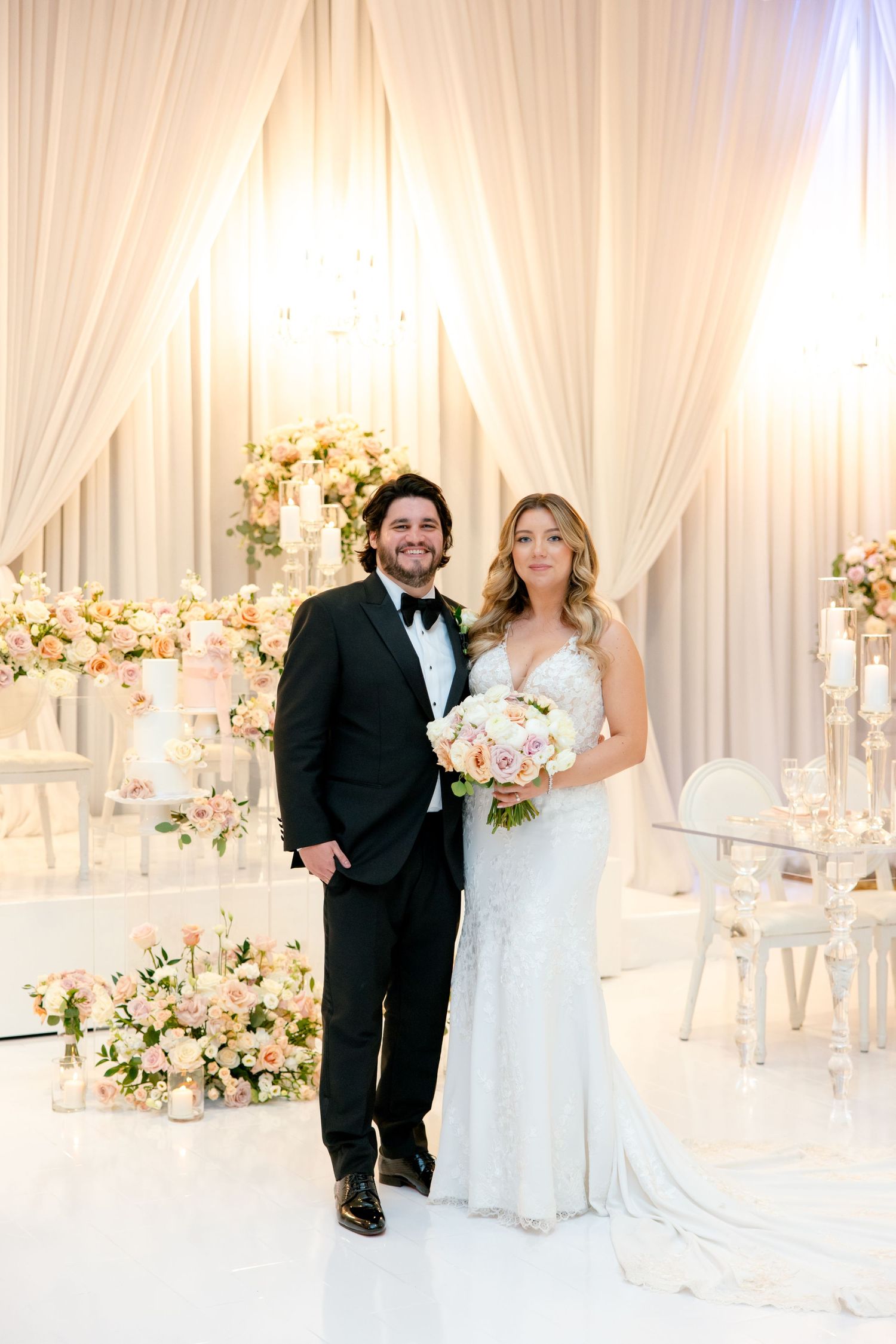 Romantic wedding portrait in white draped ballroom with floral arrangements.