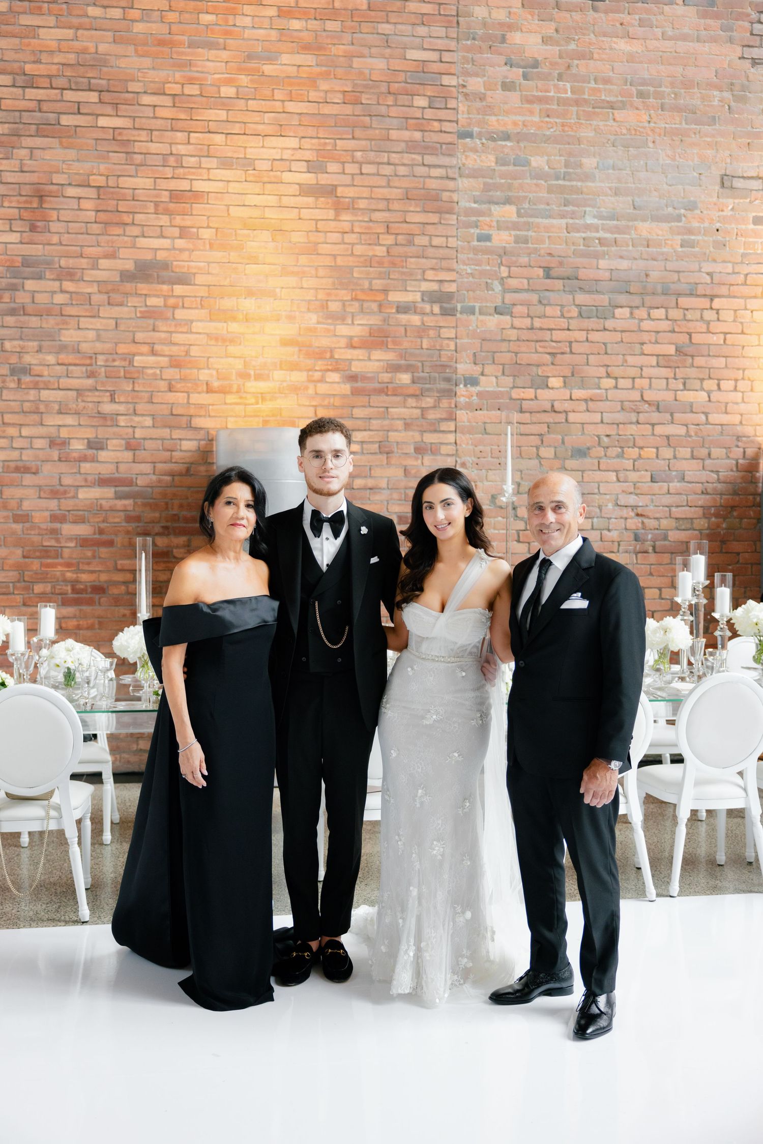 Formal wedding portrait against exposed brick wall in elegant reception venue.