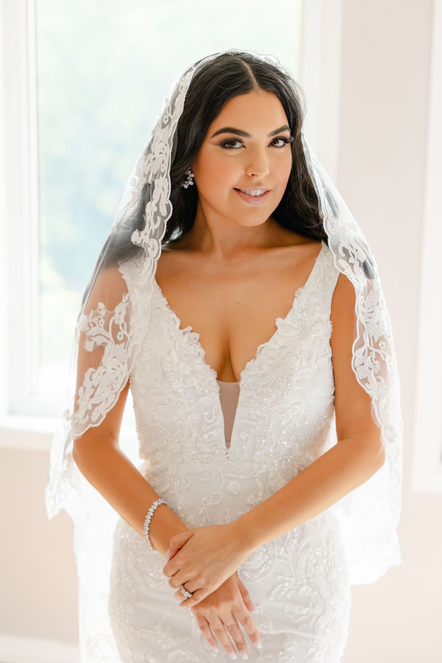 Radiant bride in form-fitting white lace gown with deep v-neckline and sheer veil.