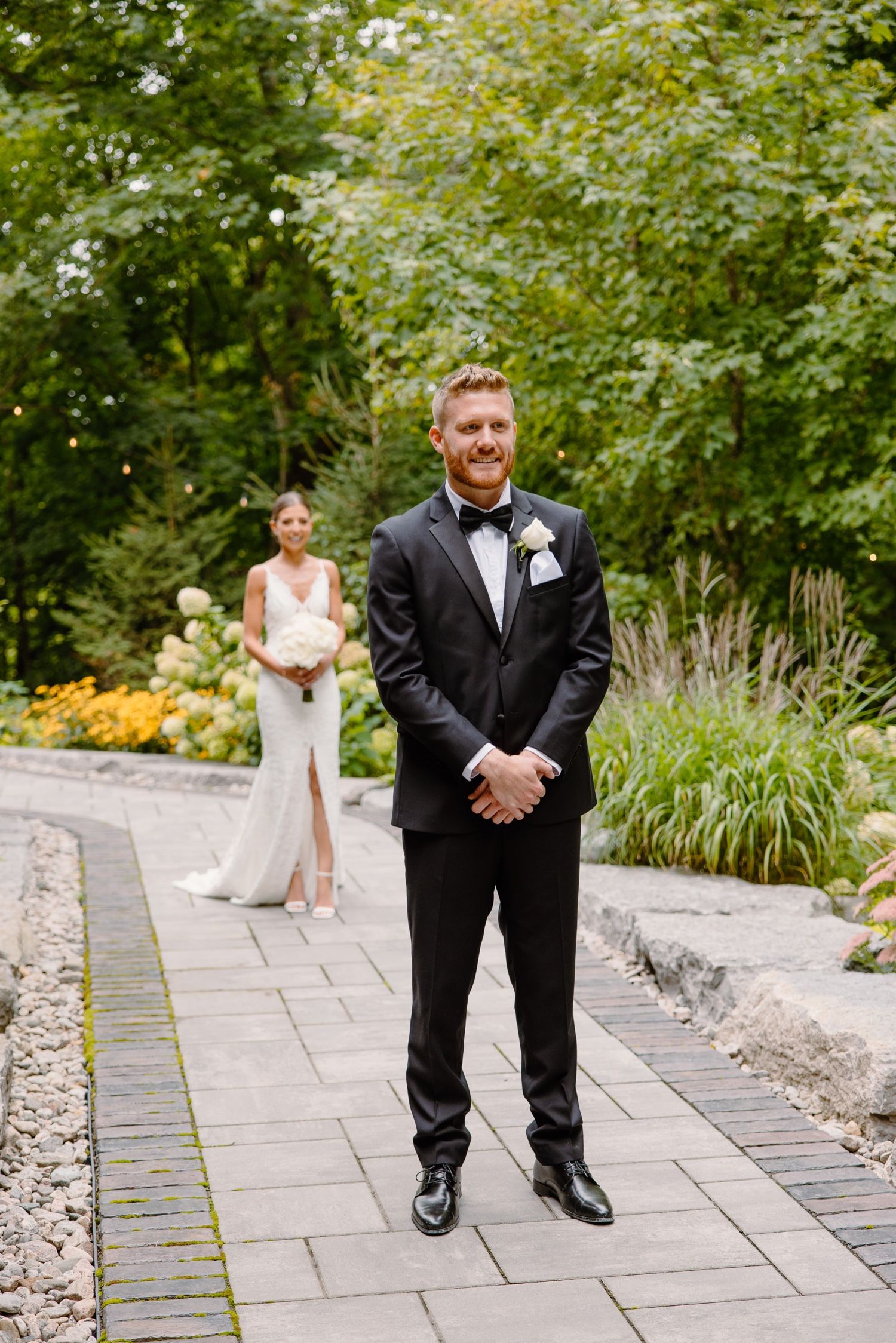 First look wedding moment on stone pathway with bride in background and groom in foreground.