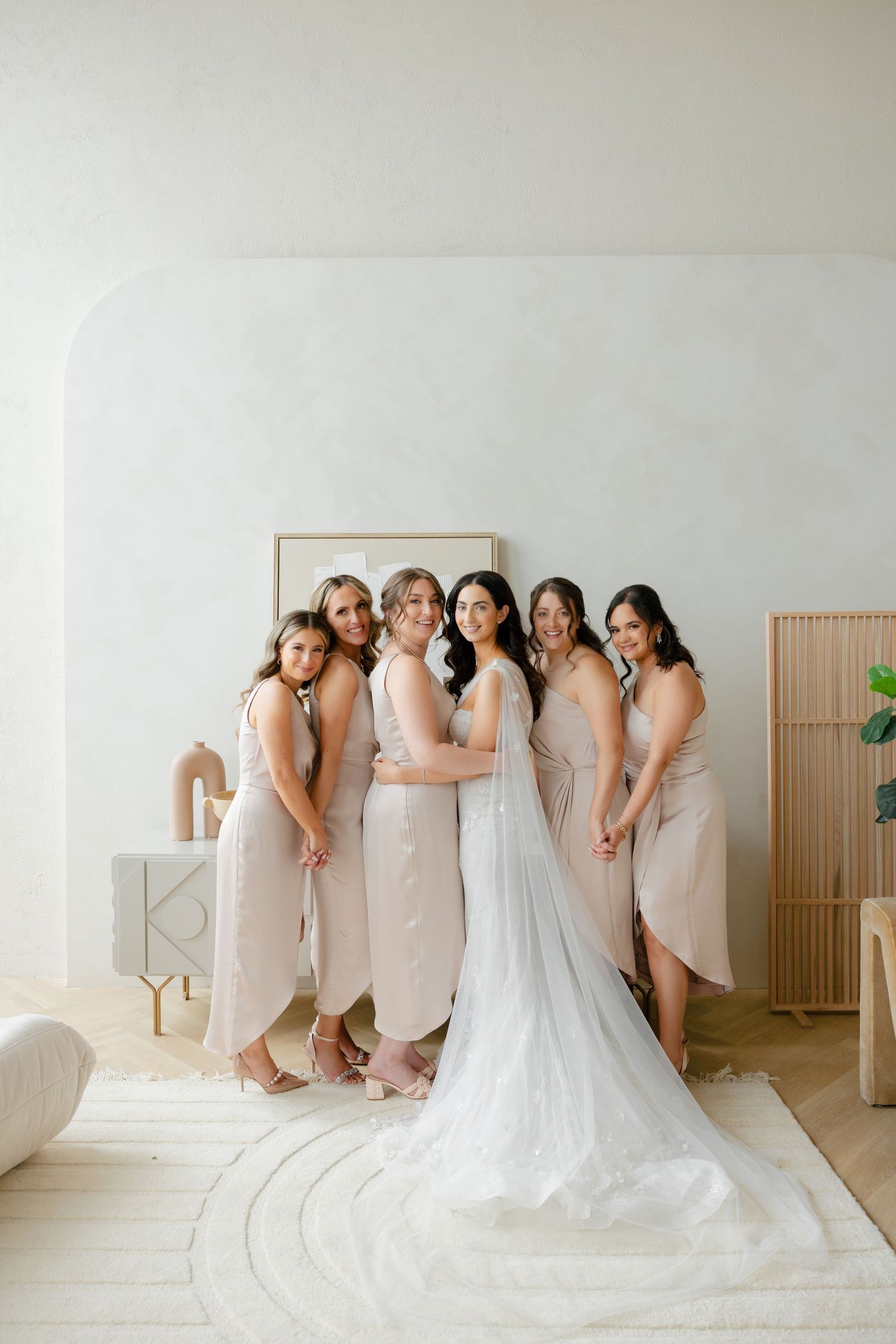 Bridesmaids in champagne dresses pose with bride in flowing white gown.