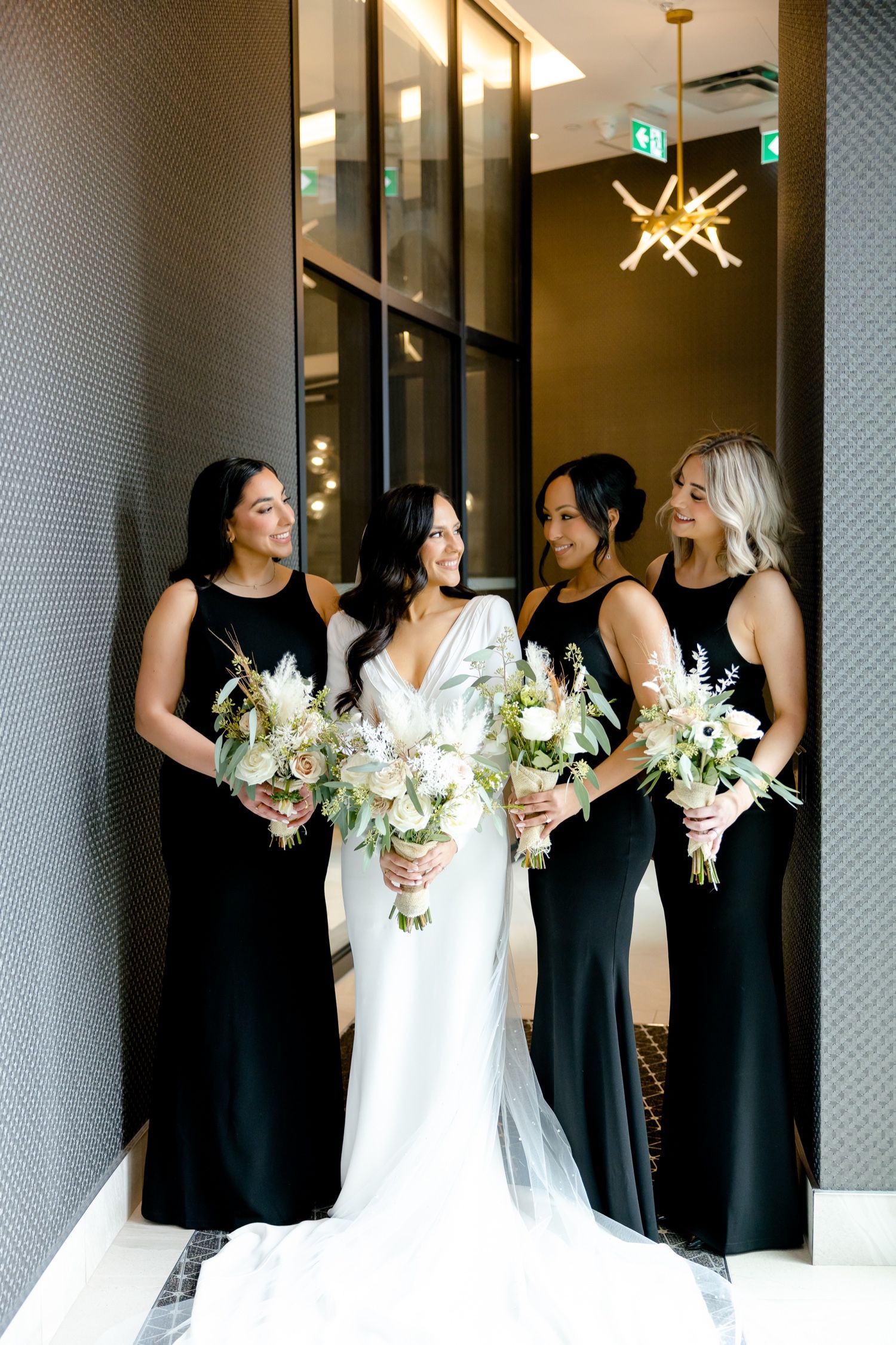Bridal party poses in modern venue with white and black gowns under artistic star-shaped chandelier.