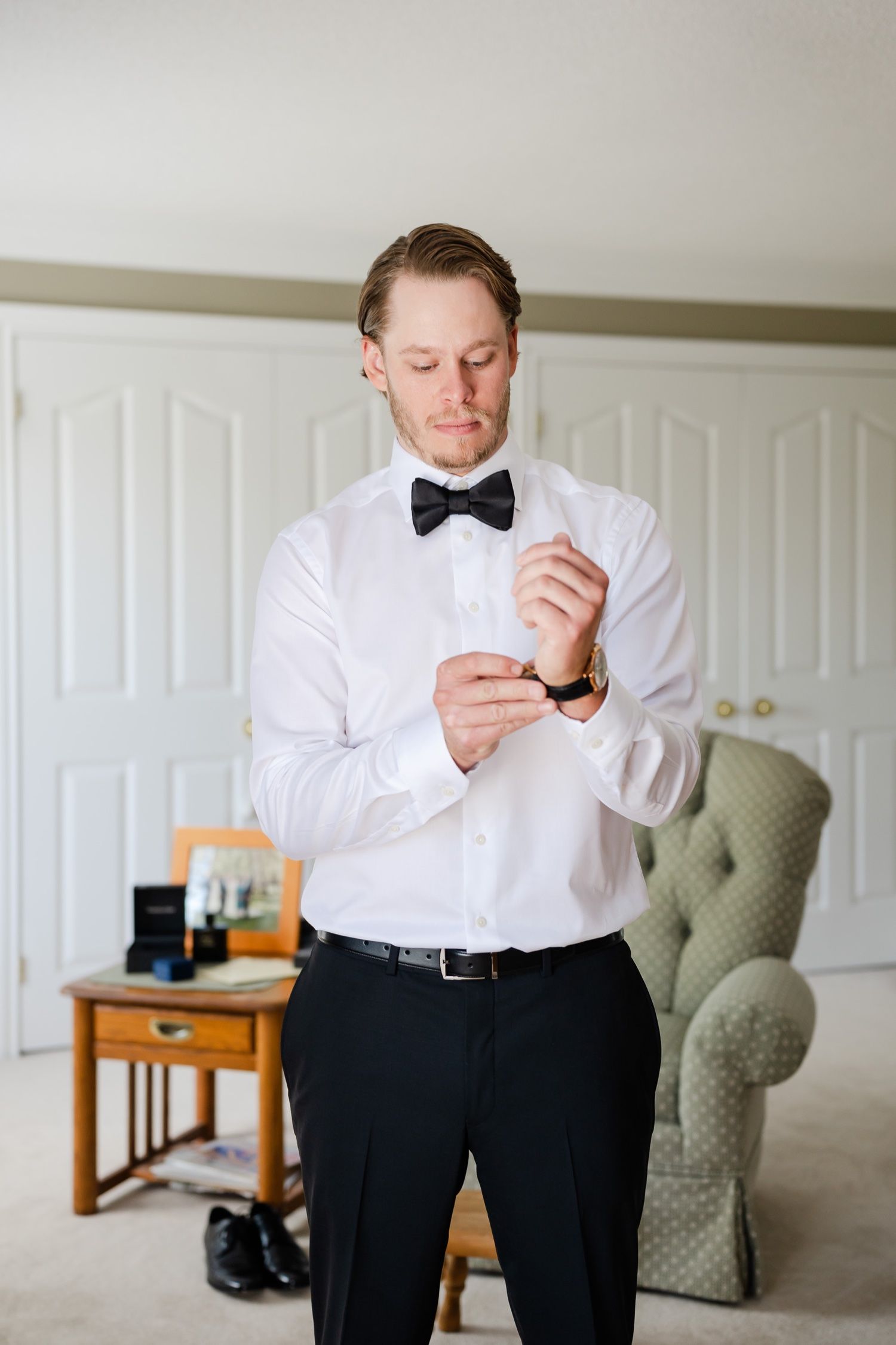 A person in formal wear adjusting their bow tie while getting ready.