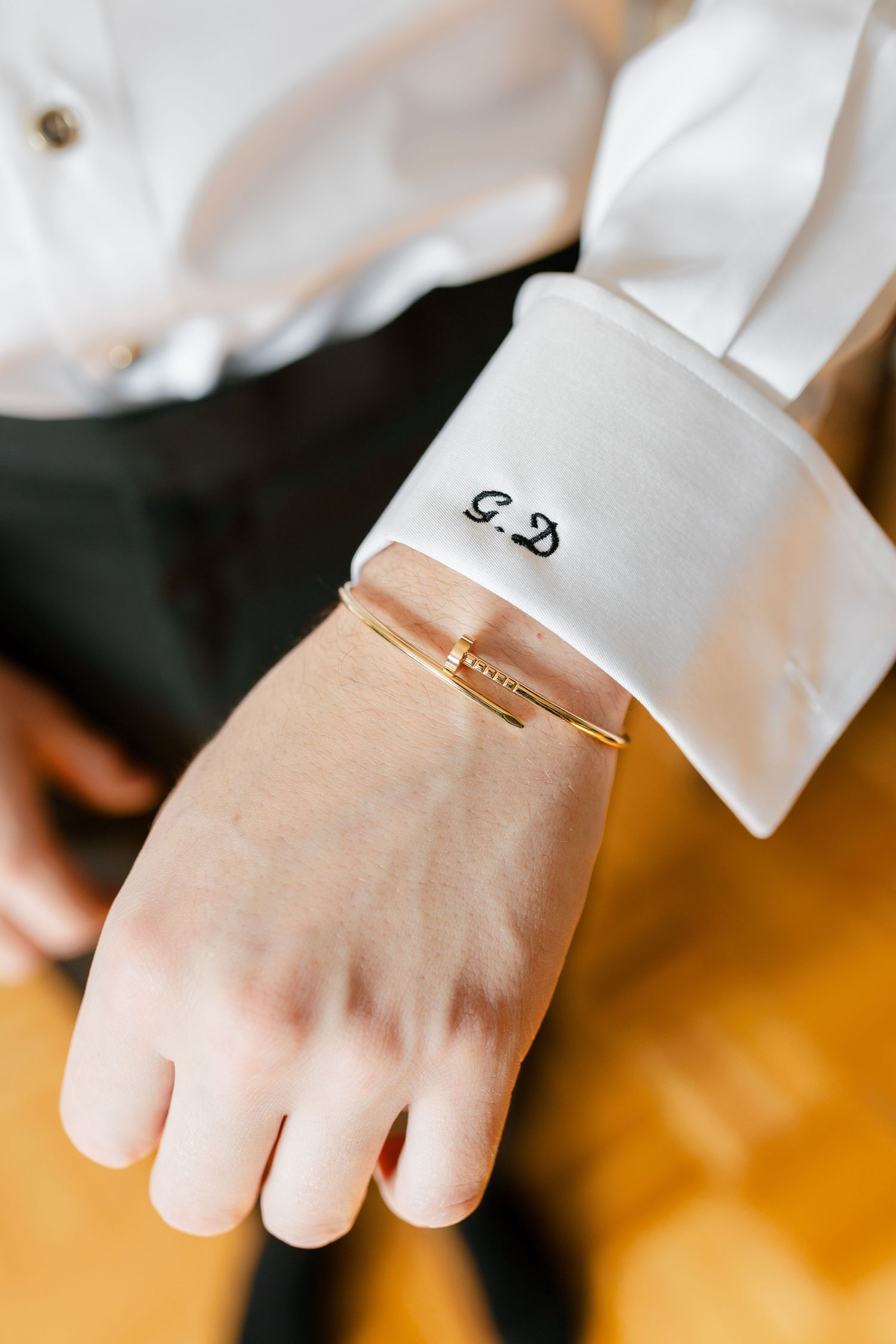 Close-up of a white dress shirt cuff with monogrammed initials and a gold bracelet.