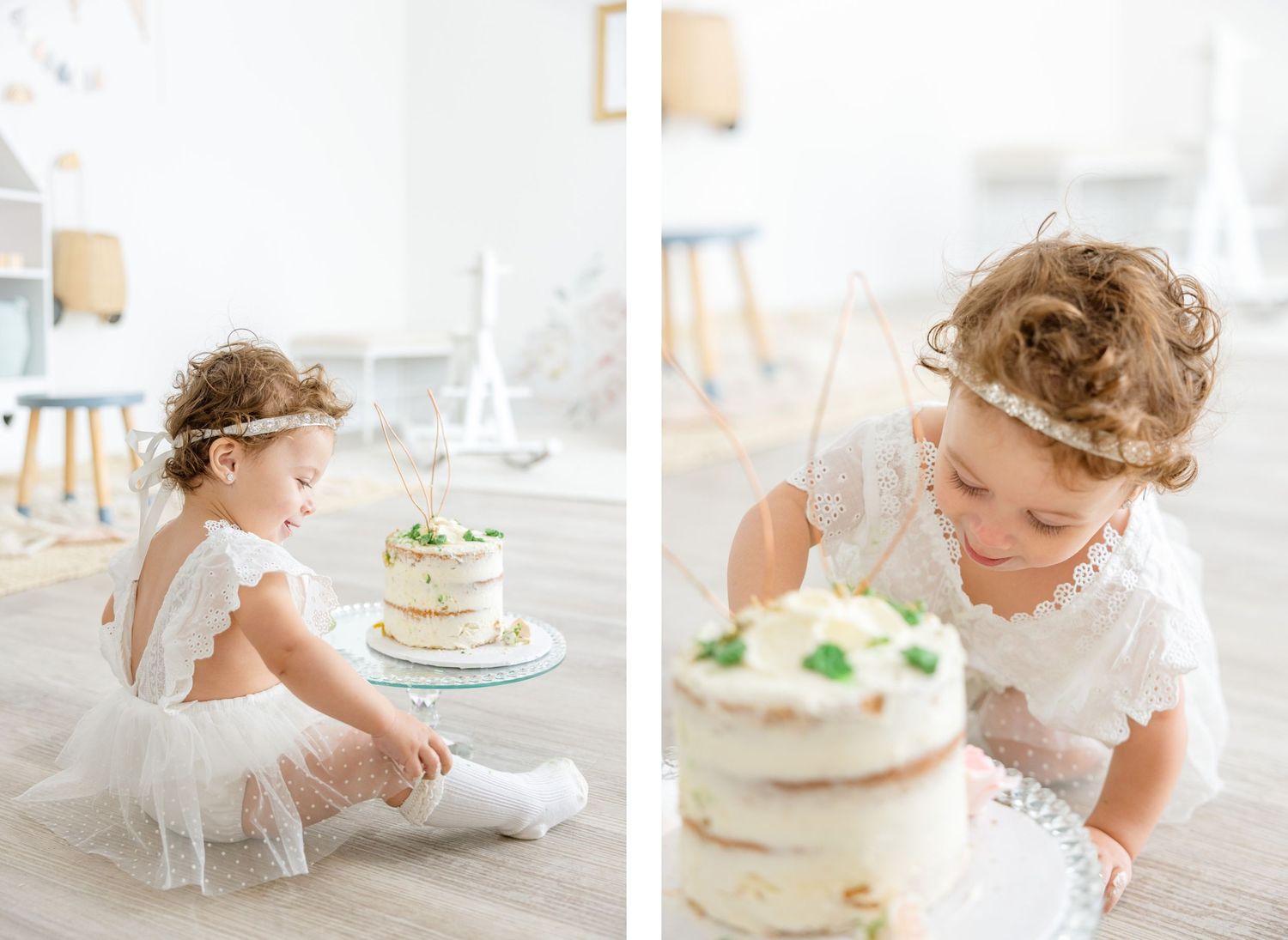 Little one in white dress explores delicate birthday cake with floral decorations.