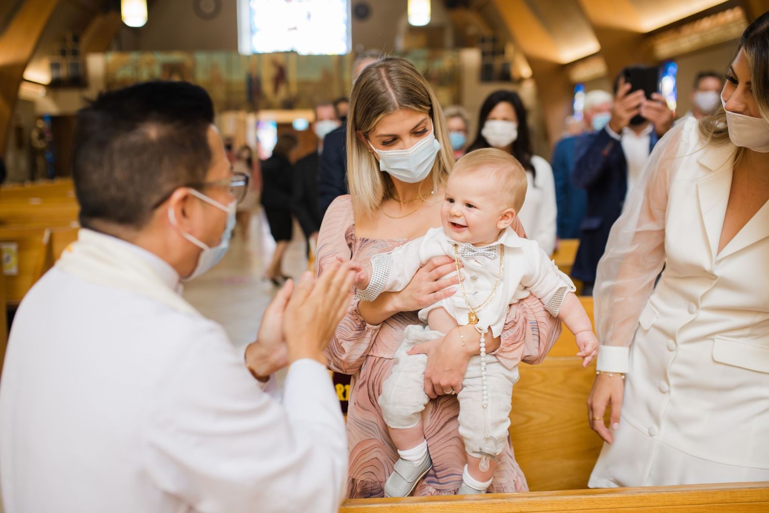 Priest blessing baby during baptism ceremony while family watches in church.