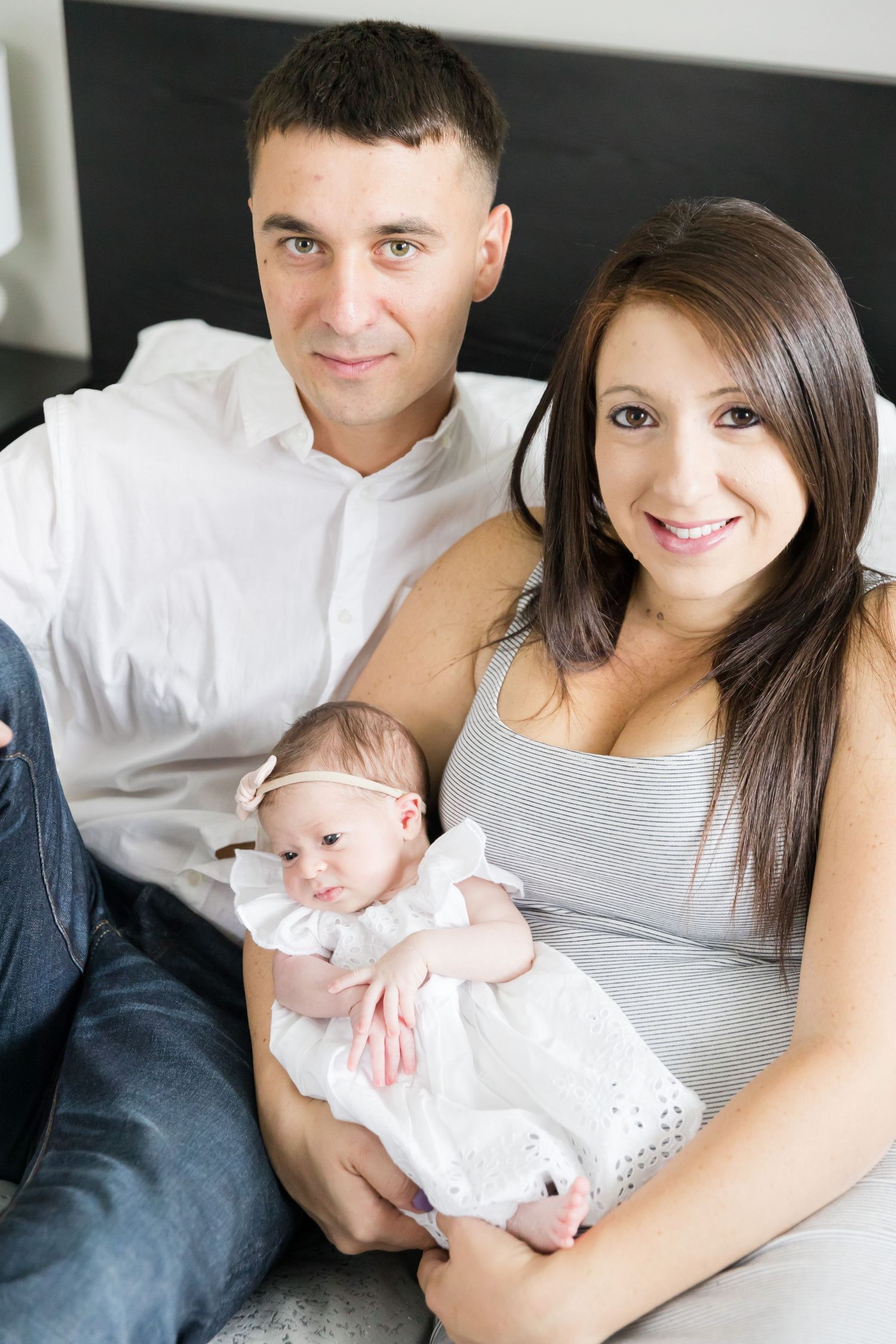 Family portrait on bed with baby wearing white dress.