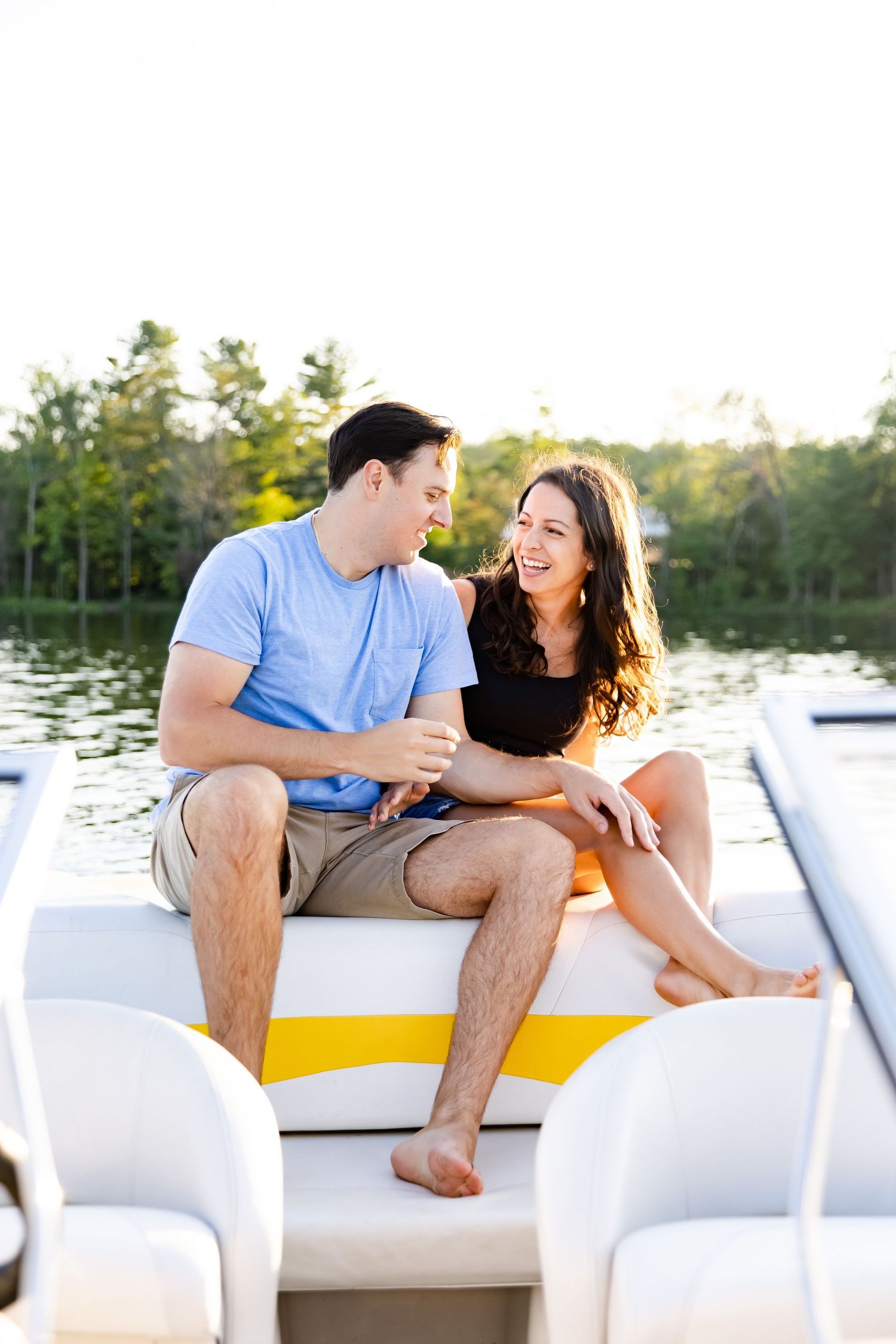 A couple laughing together while sitting on a white boat deck with a lake view.