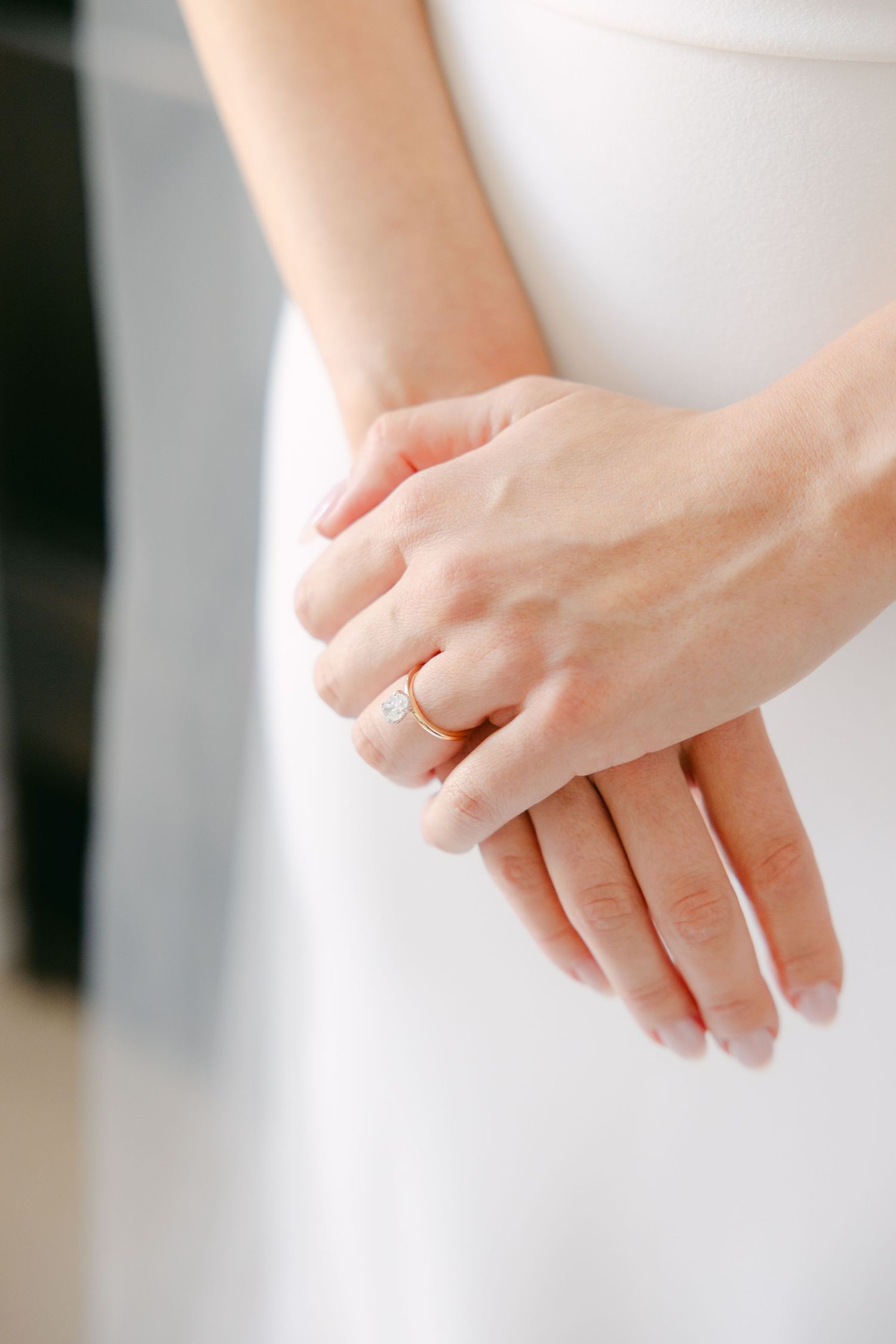 Close-up of hands showing an elegant wedding ring against a white dress.