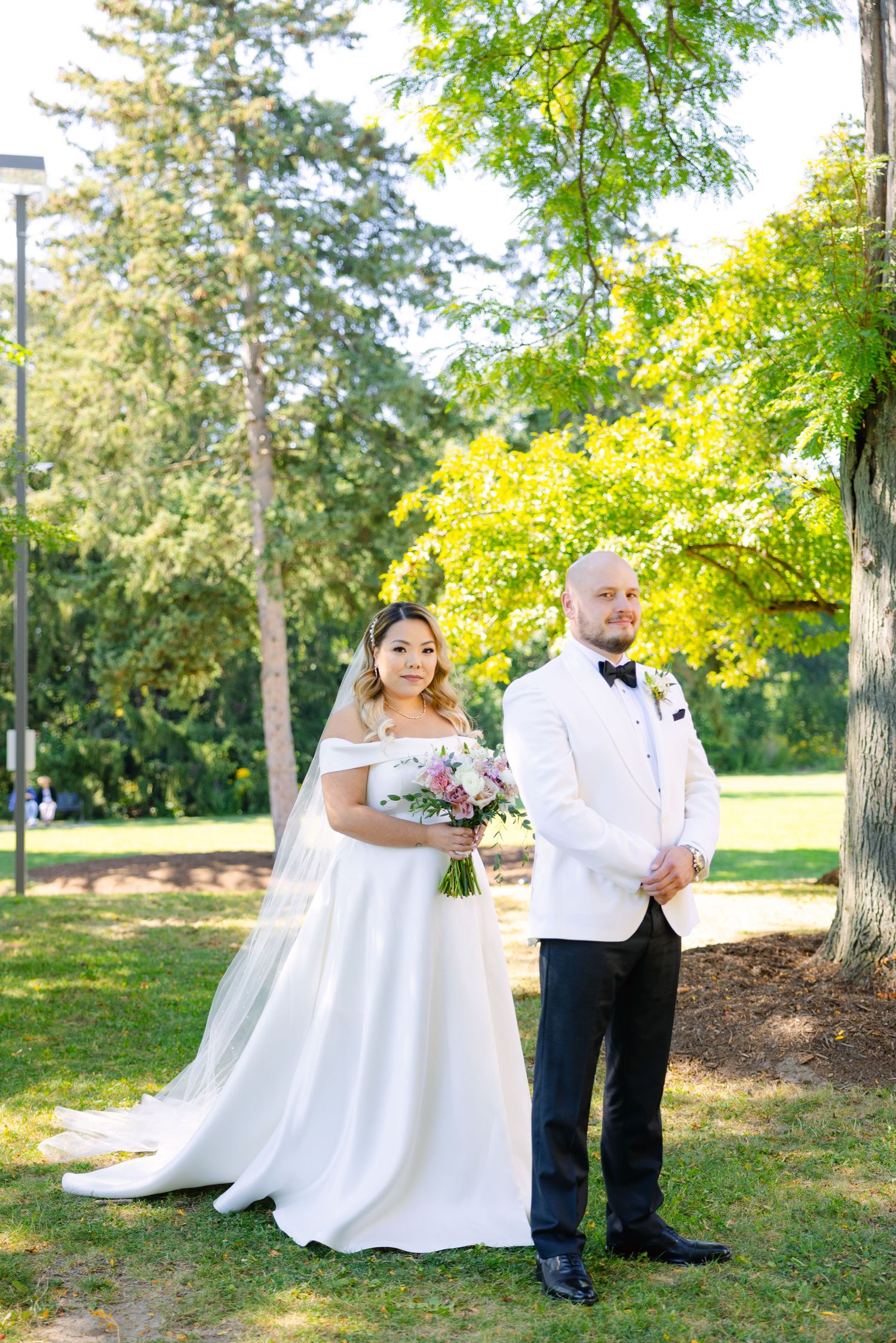 Elegant outdoor wedding portrait with couple standing among sun-dappled trees.