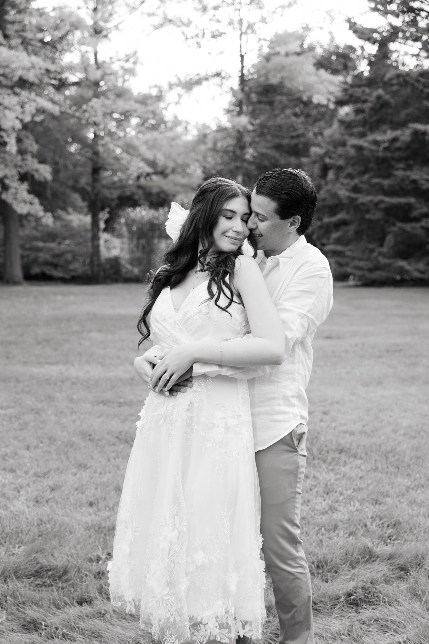 A black and white photograph showing a tender embrace between a couple in a wooded outdoor setting.