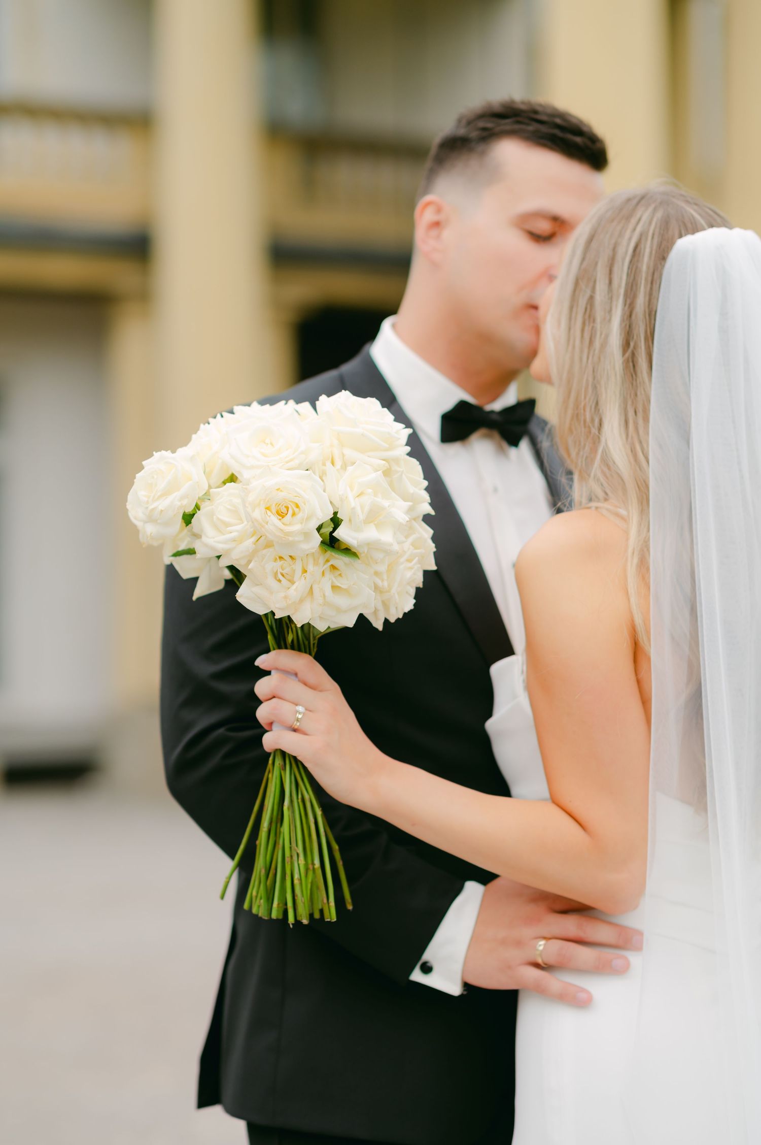 Elegant bridal portrait with white rose bouquet against neoclassical building.
