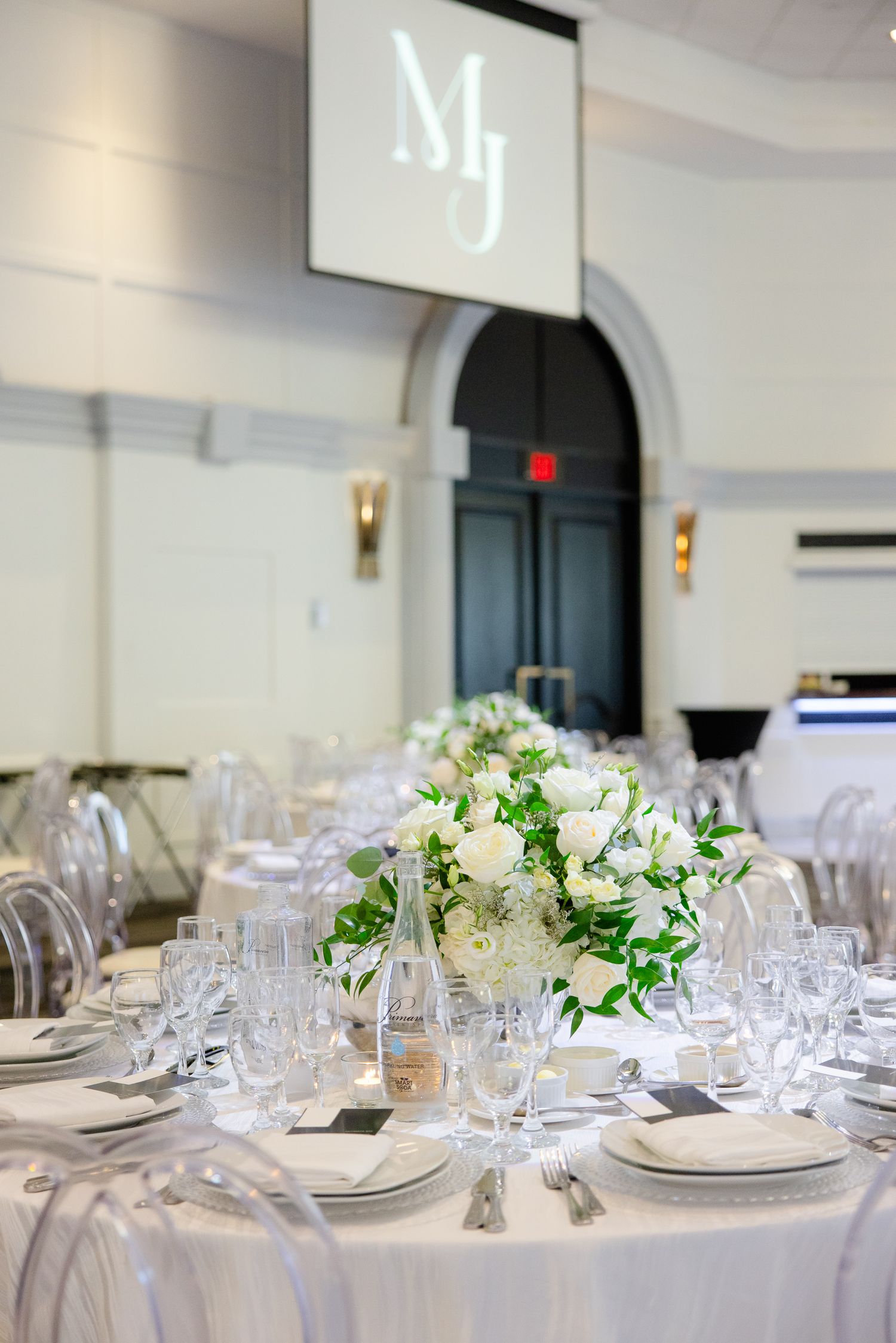 Wedding reception table with crystal glassware and lush white floral centerpiece under monogram projection.