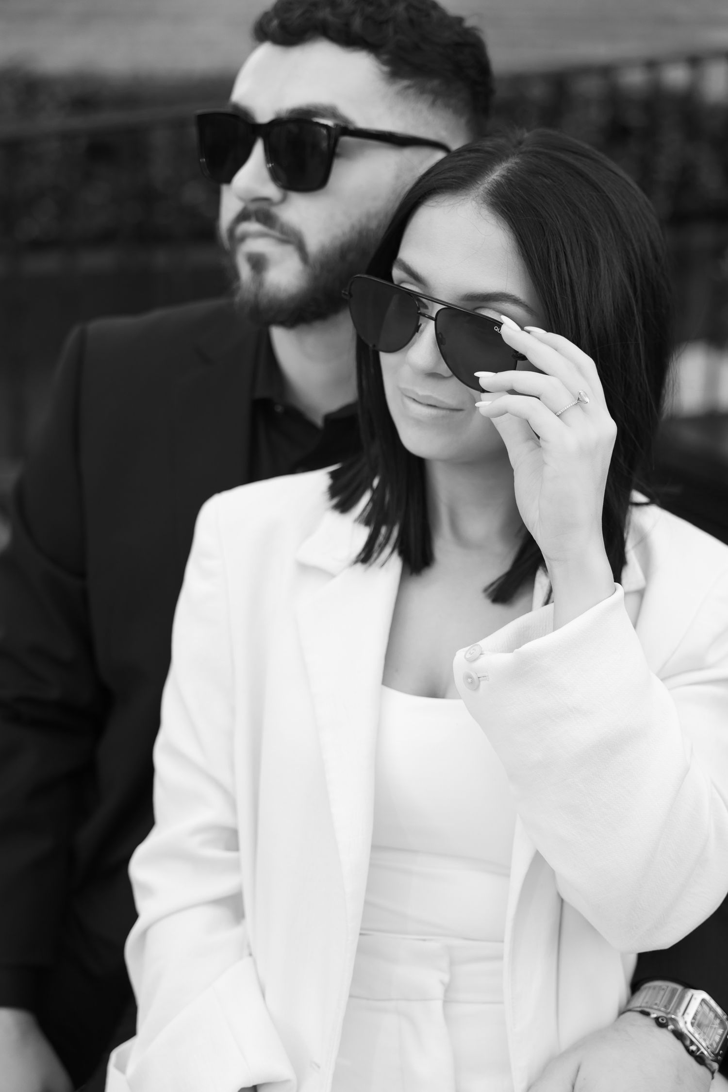 Monochrome photo of couple in designer wear adjusting sunglasses.