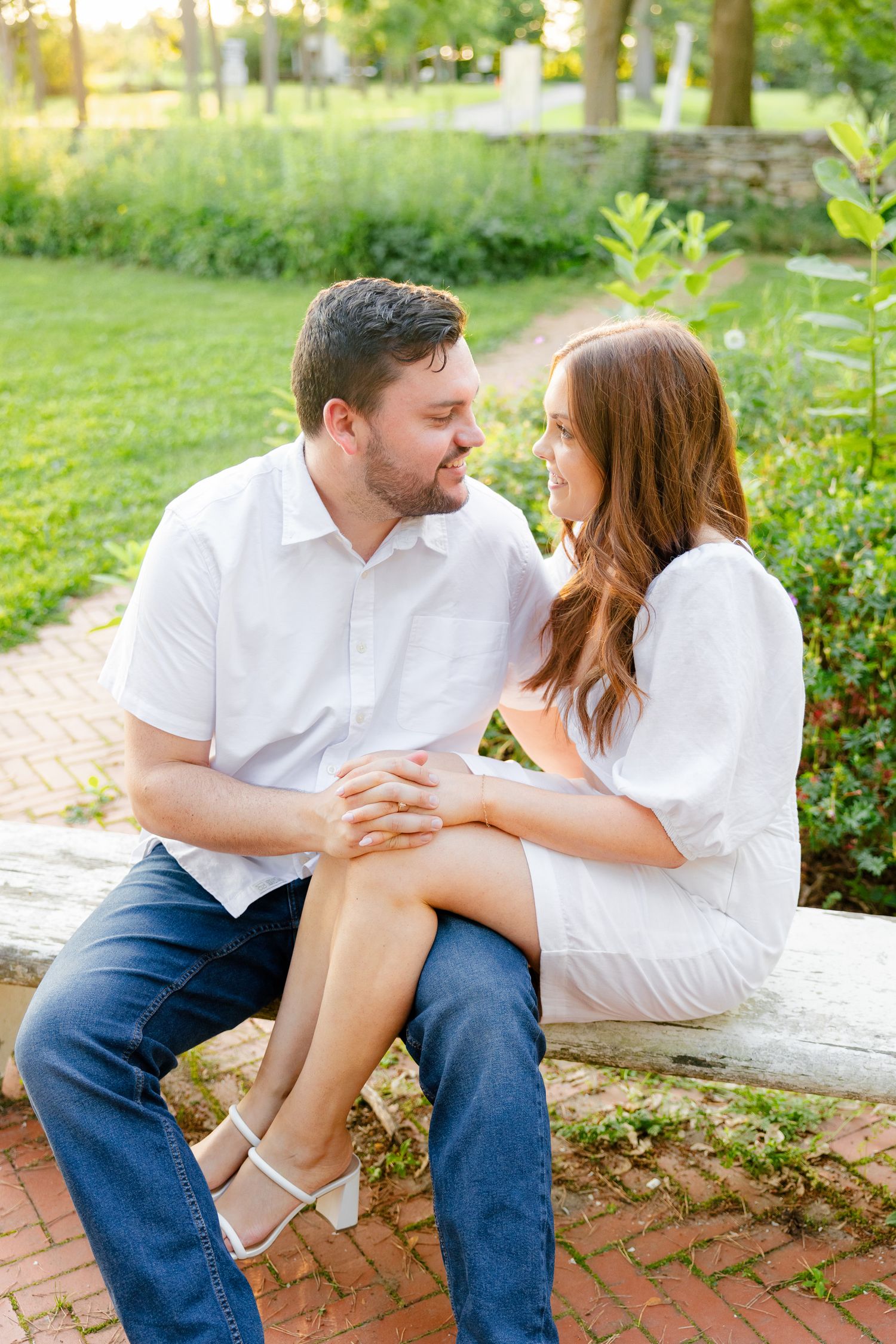 A tender moment between a couple dressed in white sitting on a brick-lined garden path.